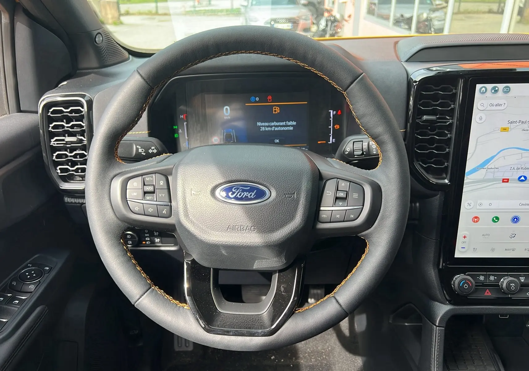 Vue rapprochée du volant noir avec surpiqûres orange du Ford Ranger 2025, affichage numérique et écran tactile de navigation.