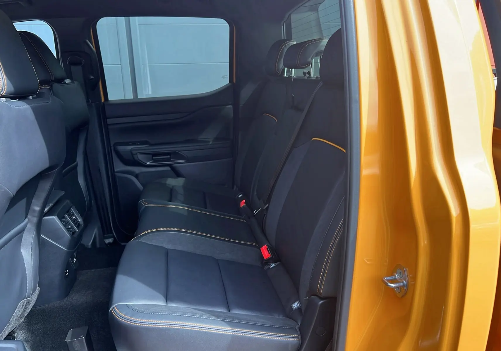 Vue intérieure côté droit sur les sièges arrière noirs avec surpiqûres orange du Ford Ranger Cyber orange 2025 Wildtrak.