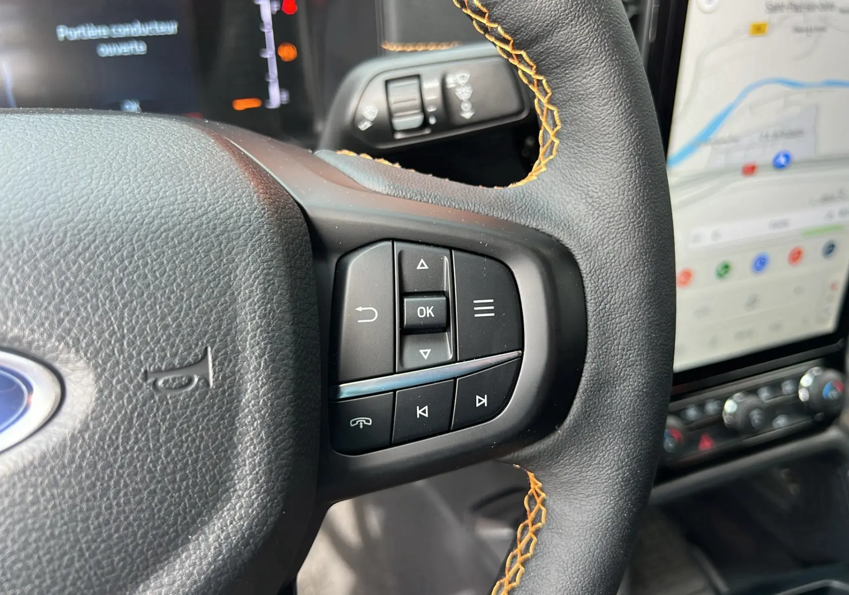 Gros plan sur le volant du Ford Ranger 2025 Cyber orange, avec surpiqûres orange et commandes intégrées.