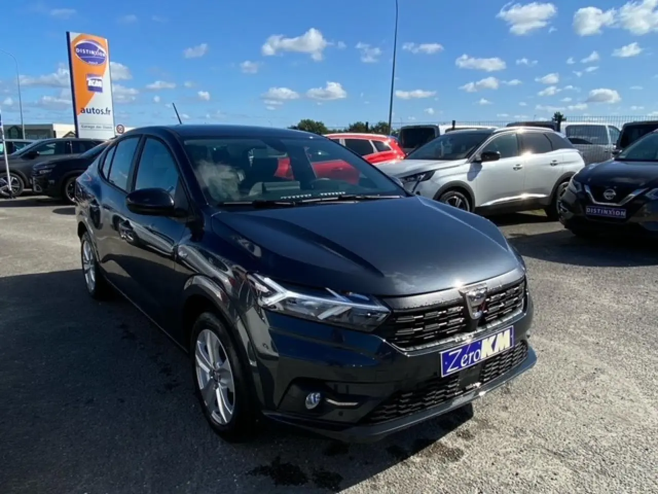 Dacia Logan gris vue 3/4 avant droit sur parking, avec calandre noire et phares LED distinctifs.
