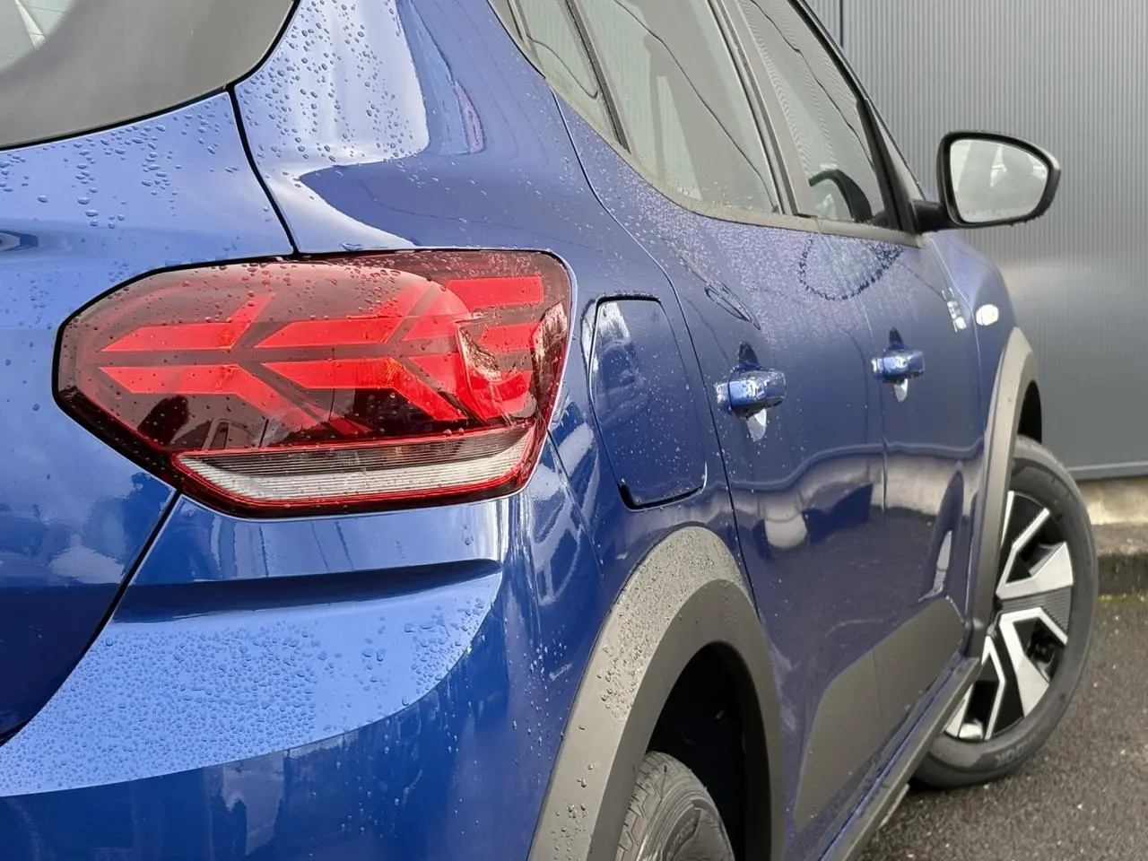 Vue 3/4 arrière droite d'une Dacia Sandero Stepway 2025 Bleu Iron avec feux arrière en Y et jantes spécifiques.