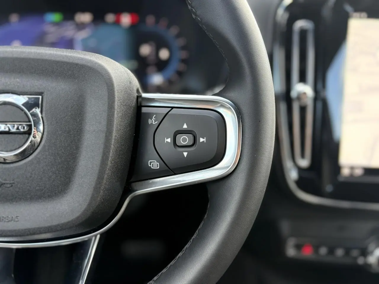 Gros plan sur le côté droit du volant noir du Volvo XC40 rouge Fusion 2024 avec commandes intégrées et logo central visible.