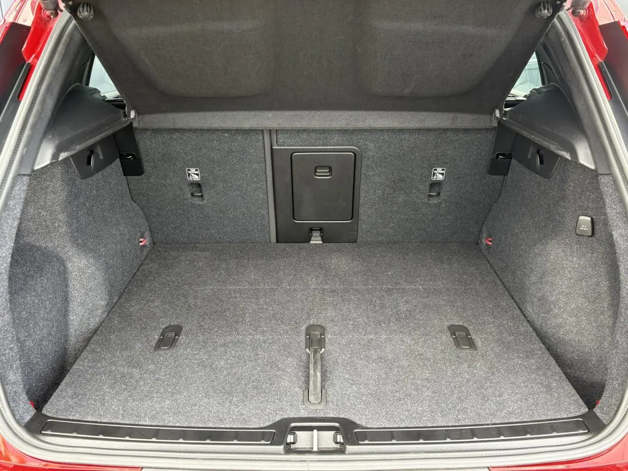 Coffre ouvert du Volvo XC40 B3 MHEV rouge Fusion, montrant l'espace de chargement et la moquette grise.