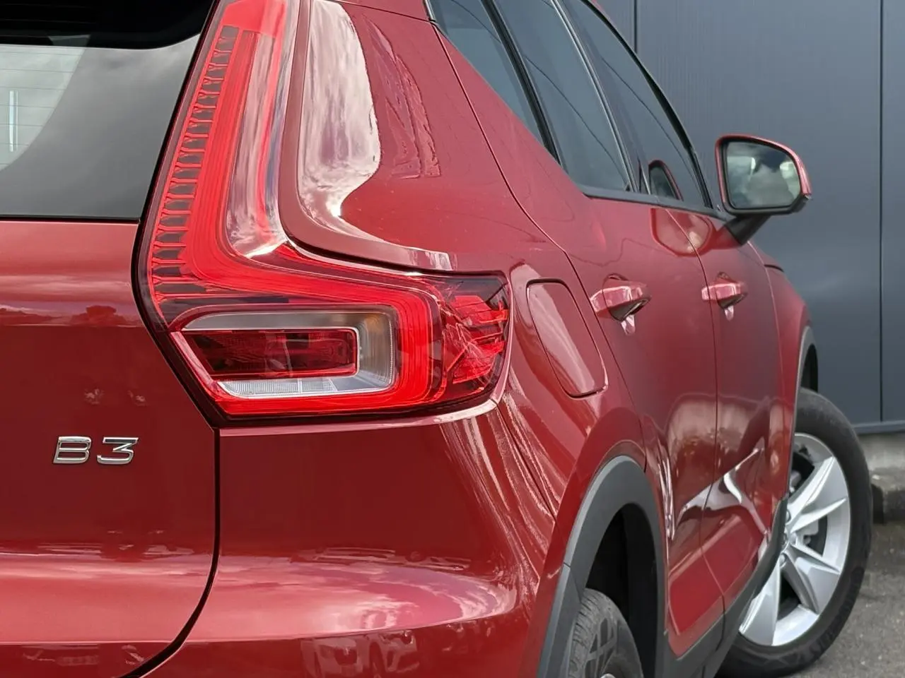 Vue 3/4 arrière droit du Volvo XC40 B3 MHEV rouge Fusion, mettant en valeur le feu arrière et la jante alliage 18 pouces.