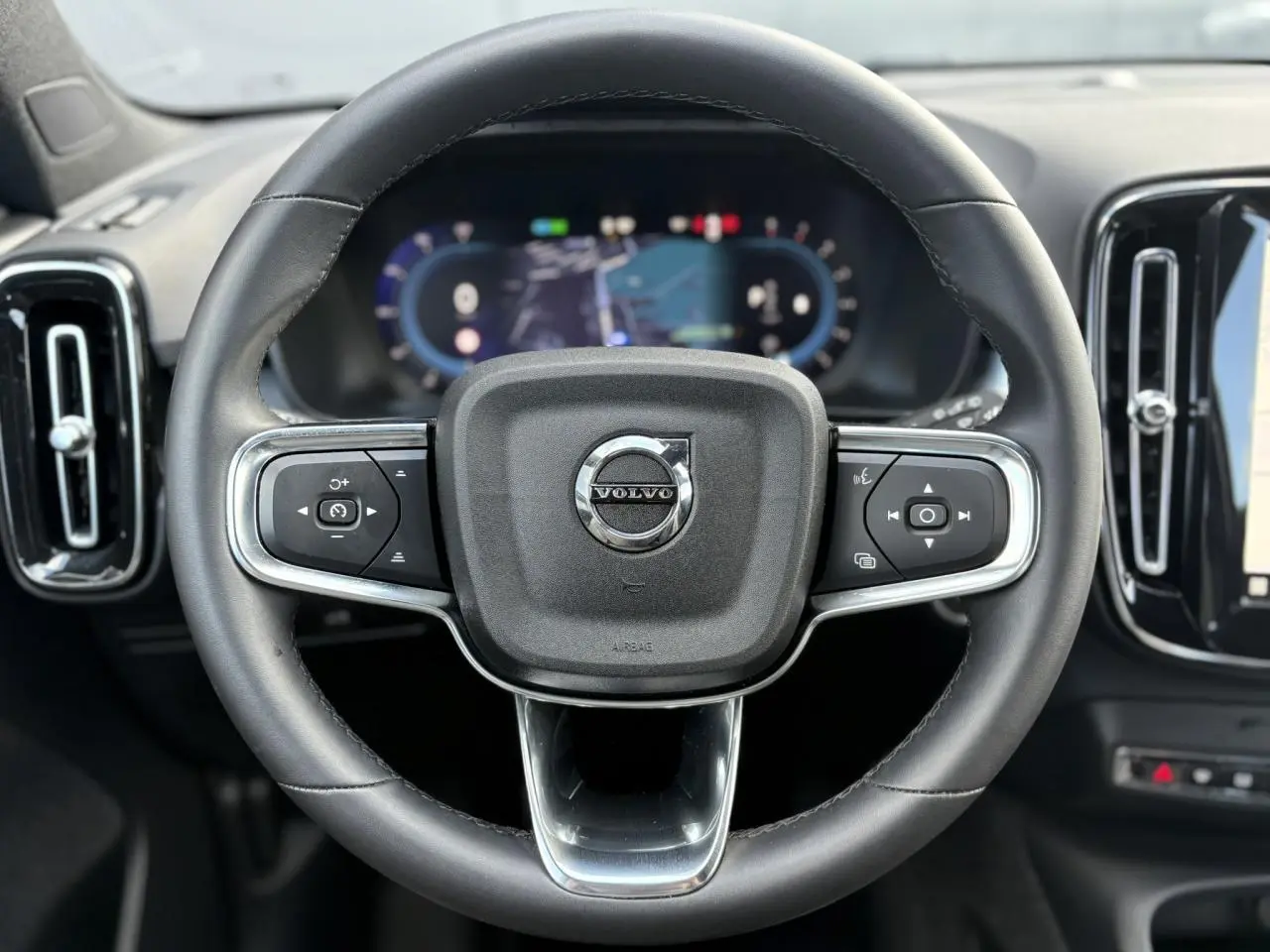 Volant cuir noir Volvo XC40 2024 vu de face avec commandes intégrées et tableau de bord digital flou.