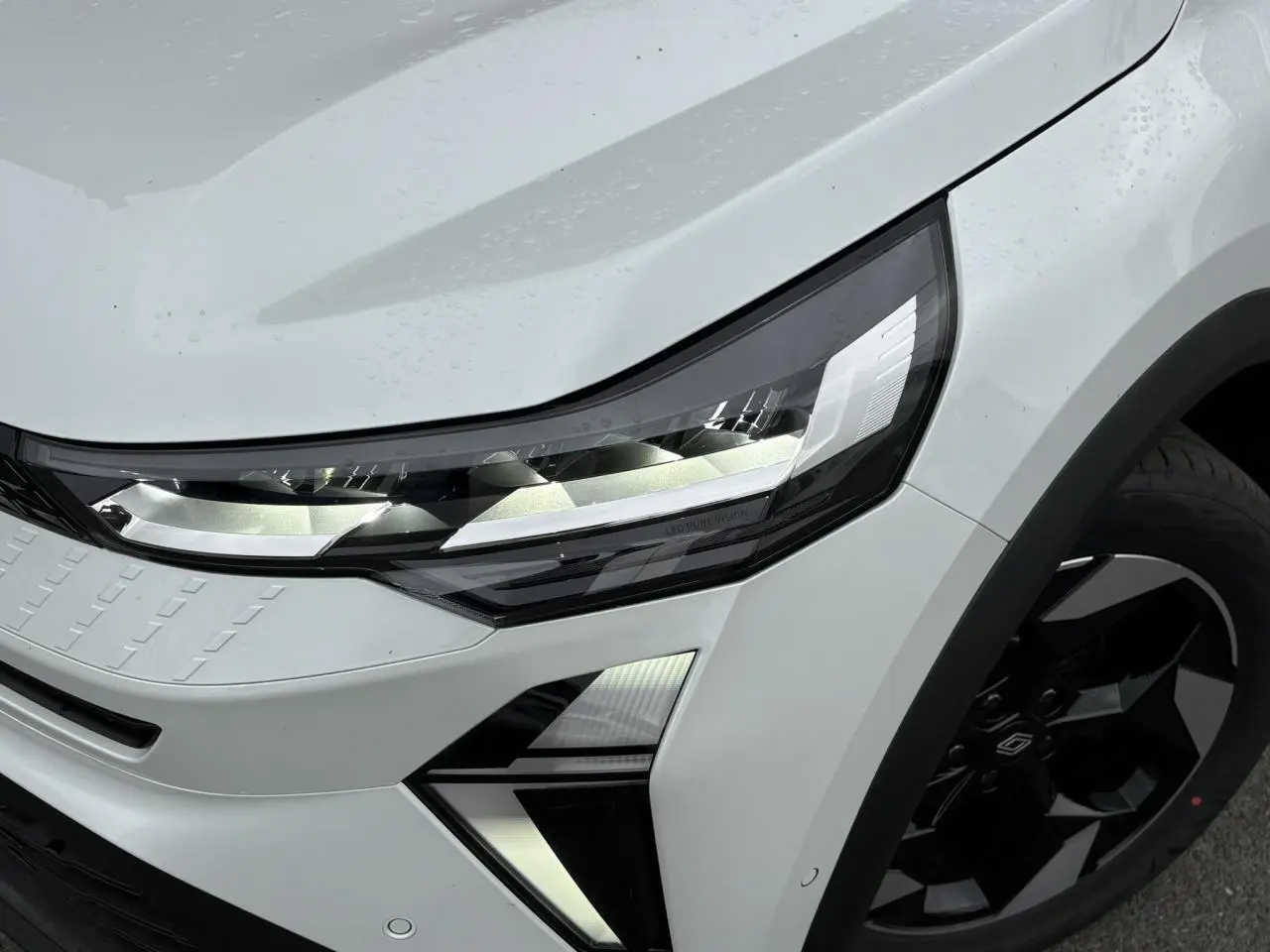 Gros plan sur l'avant droit du Renault Captur blanc nacré, mettant en valeur le phare LED et la jante noire.