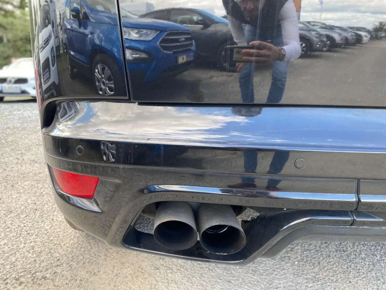 Gros plan sur la double sortie d’échappement arrière droite du Range Rover Sport noir, avec reflet du photographe sur la carrosserie.