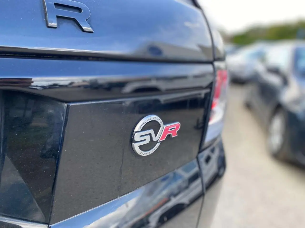 Gros plan sur l'arrière noir brillant d'un Range Rover Sport SVR avec le badge SVR rouge et argent visible.