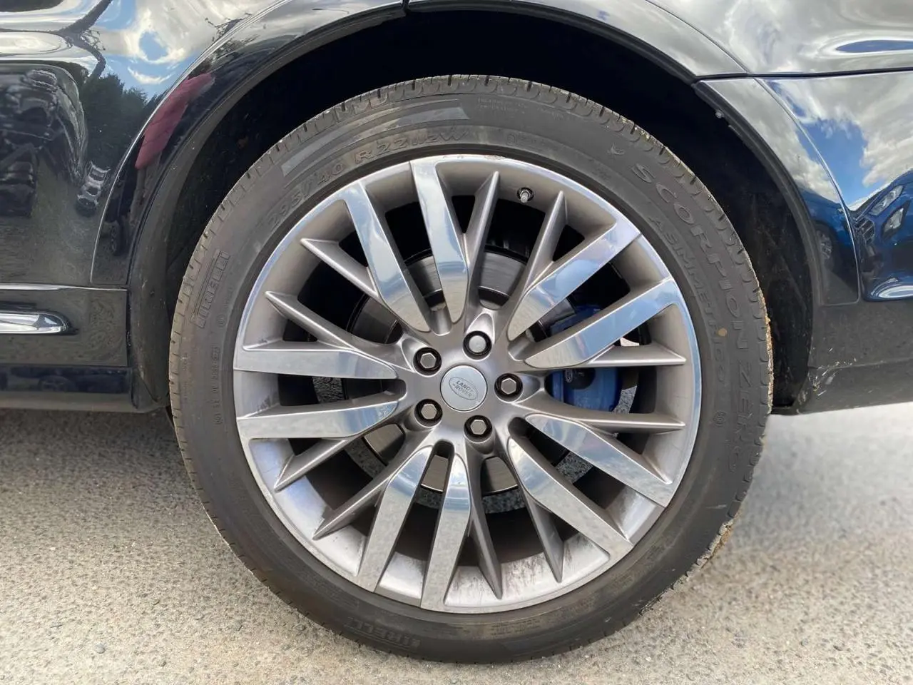 Gros plan sur la jante 22 pouces argentée et l'étrier de frein bleu du Range Rover Sport noir côté gauche.