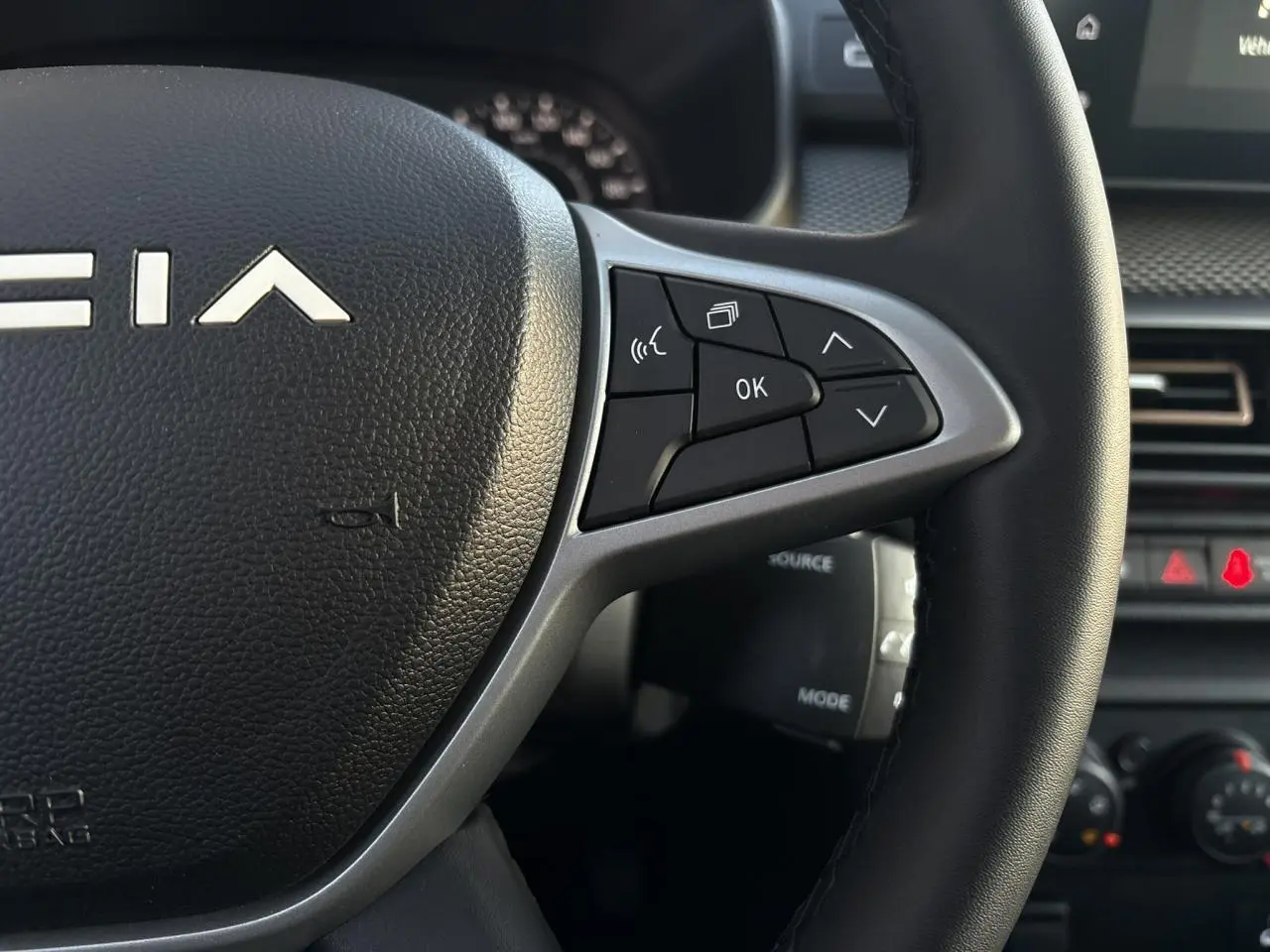 Gros plan sur le volant noir de la Dacia Sandero Stepway 2025 avec commandes multifonctions et logo central blanc.