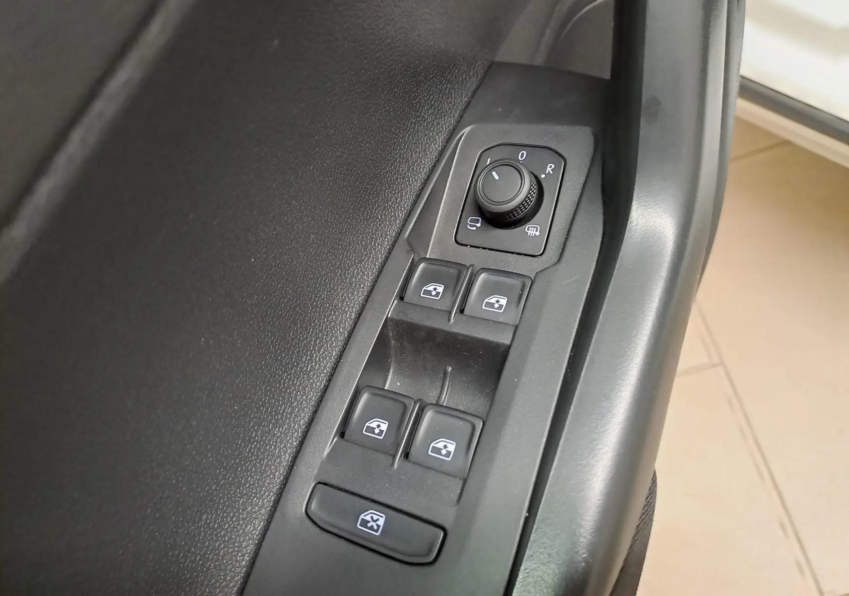 Gros plan sur les commandes de lève-vitres et réglage des rétroviseurs côté conducteur du Volkswagen Taigo blanc 2024.