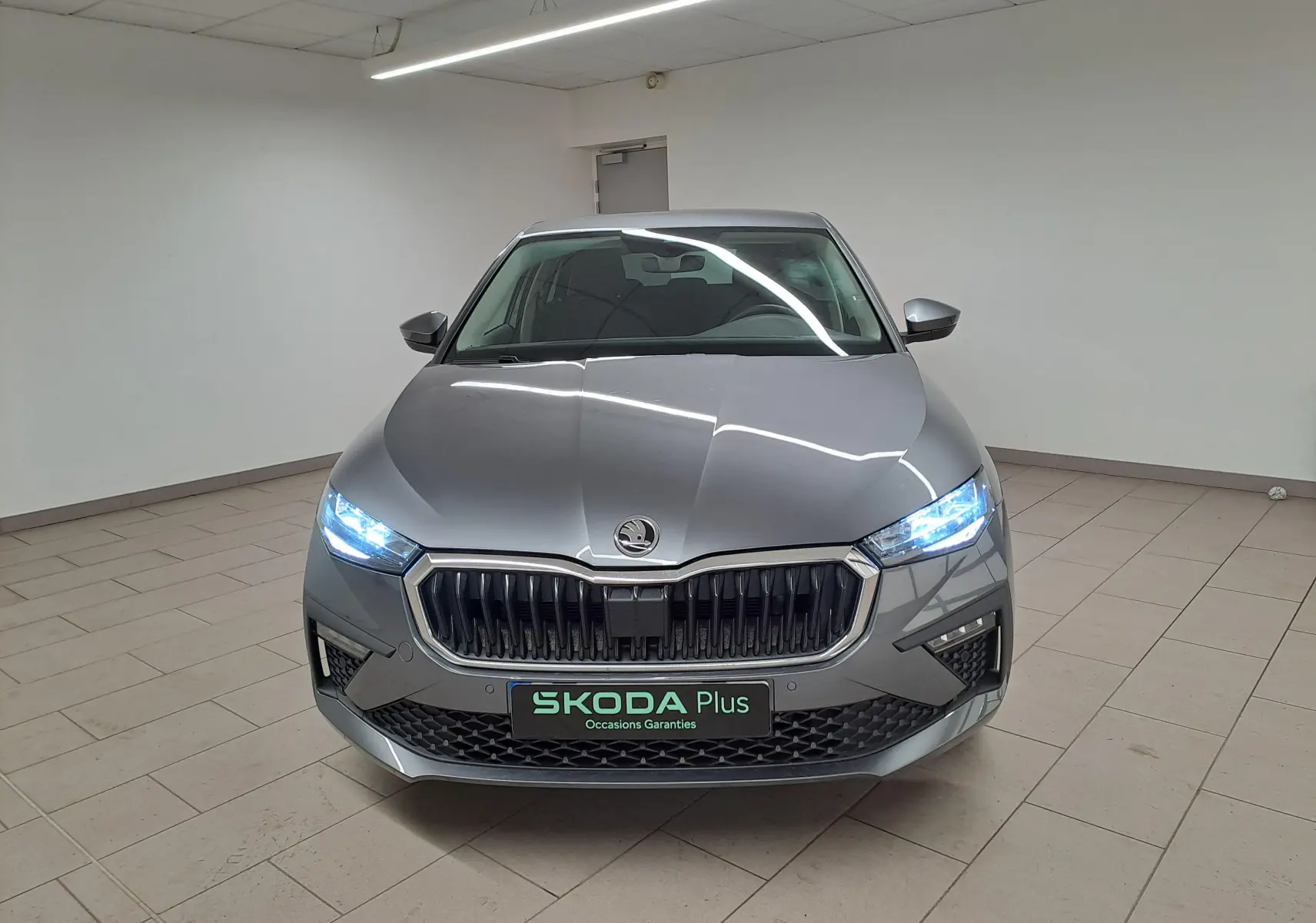 Vue frontale d'une Skoda Scala 2025 gris graphite avec phares allumés et calandre marquée SKODA Plus.