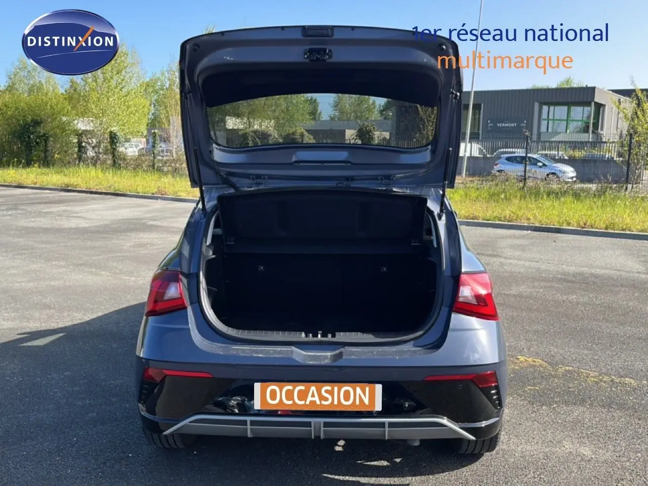 Vue arrière d'une Hyundai i20 gris Aurora Metal 2025 avec coffre ouvert sur un parking extérieur.