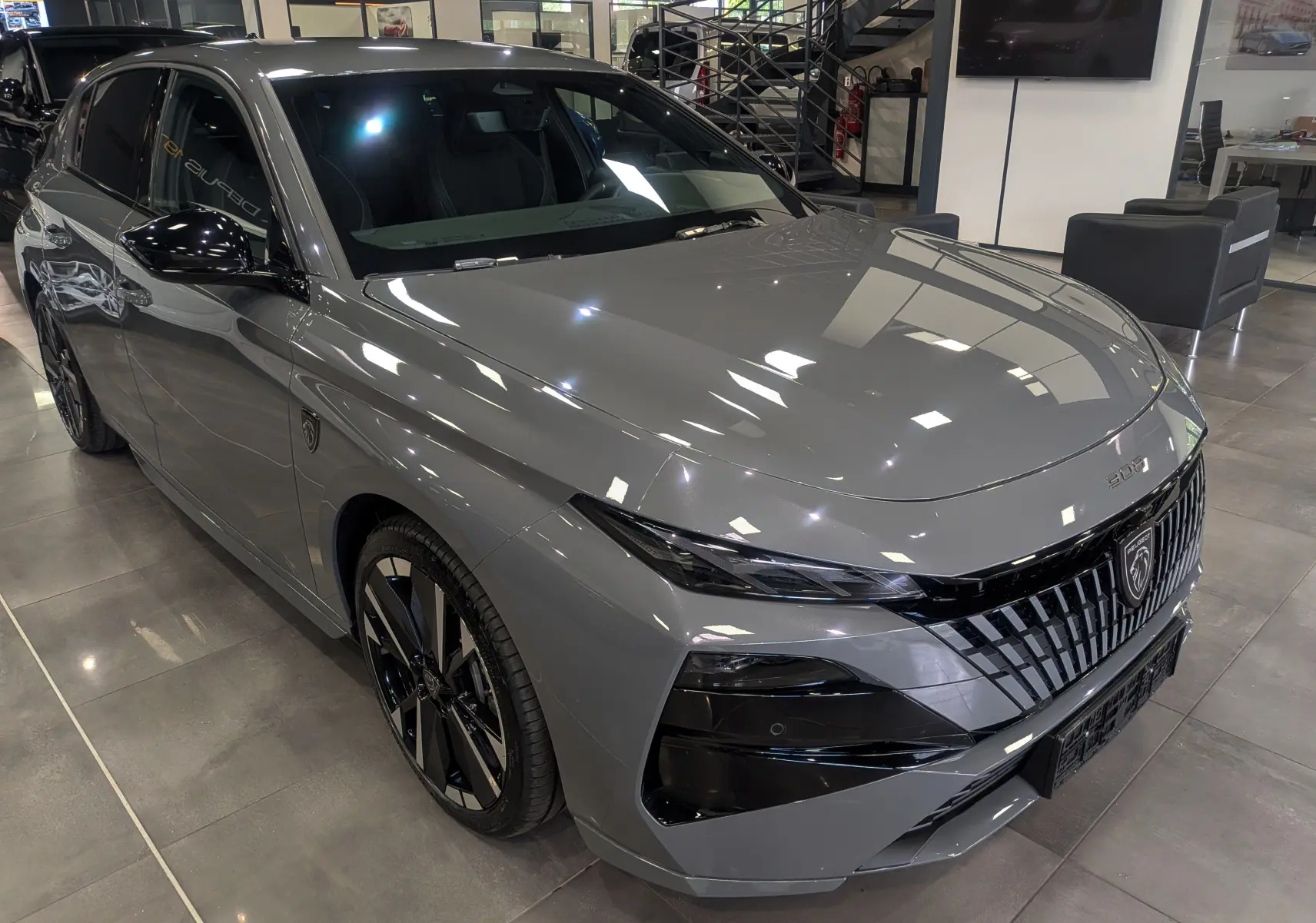 Peugeot 308 gris Sélénium vue 3/4 avant droit en showroom, avec calandre noire distinctive et jantes bicolores.