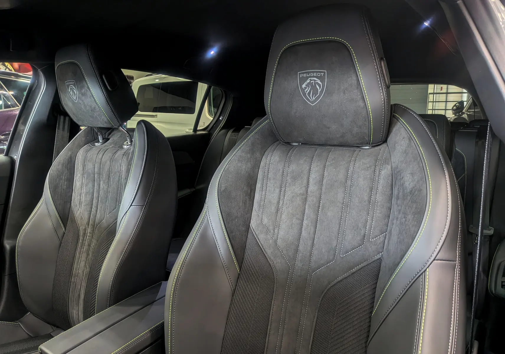 Gros plan sur les sièges avant en cuir noir et alcantara avec surpiqûres vertes et logo Peugeot embossé.