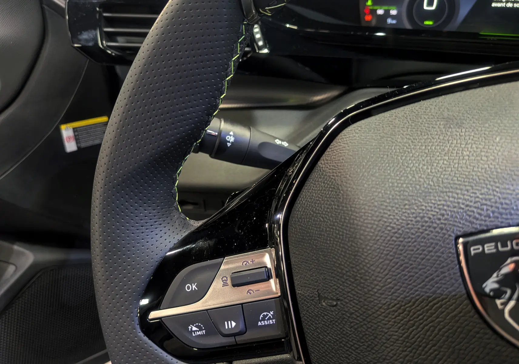Gros plan sur le volant cuir noir perforé de la Peugeot 308 GT Exclusive 2026 avec commandes intégrées et logo lion.
