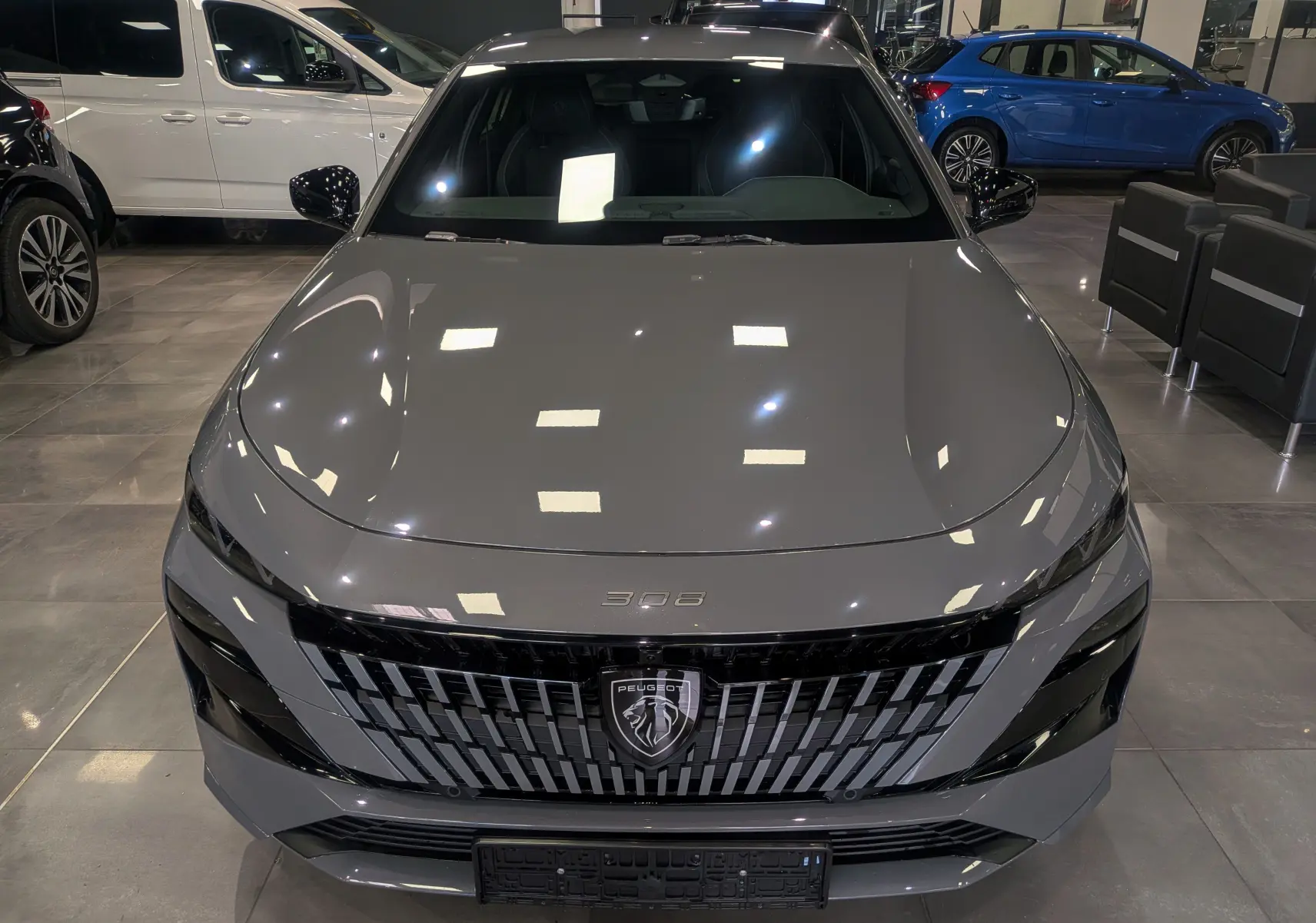 Vue avant frontale d'une Peugeot 308 gris Sélénium avec calandre noire distinctive en showroom.