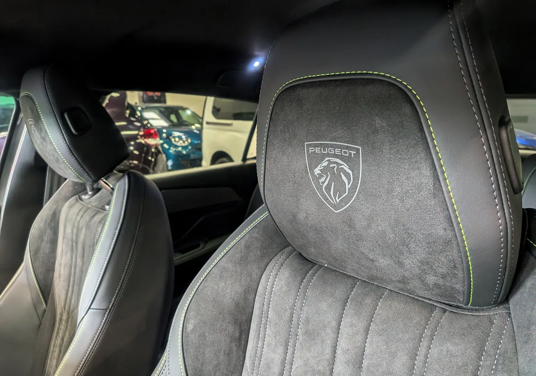 Gros plan sur les sièges avant en cuir noir et alcantara gris avec logo Peugeot brodé et surpiqûres vertes.