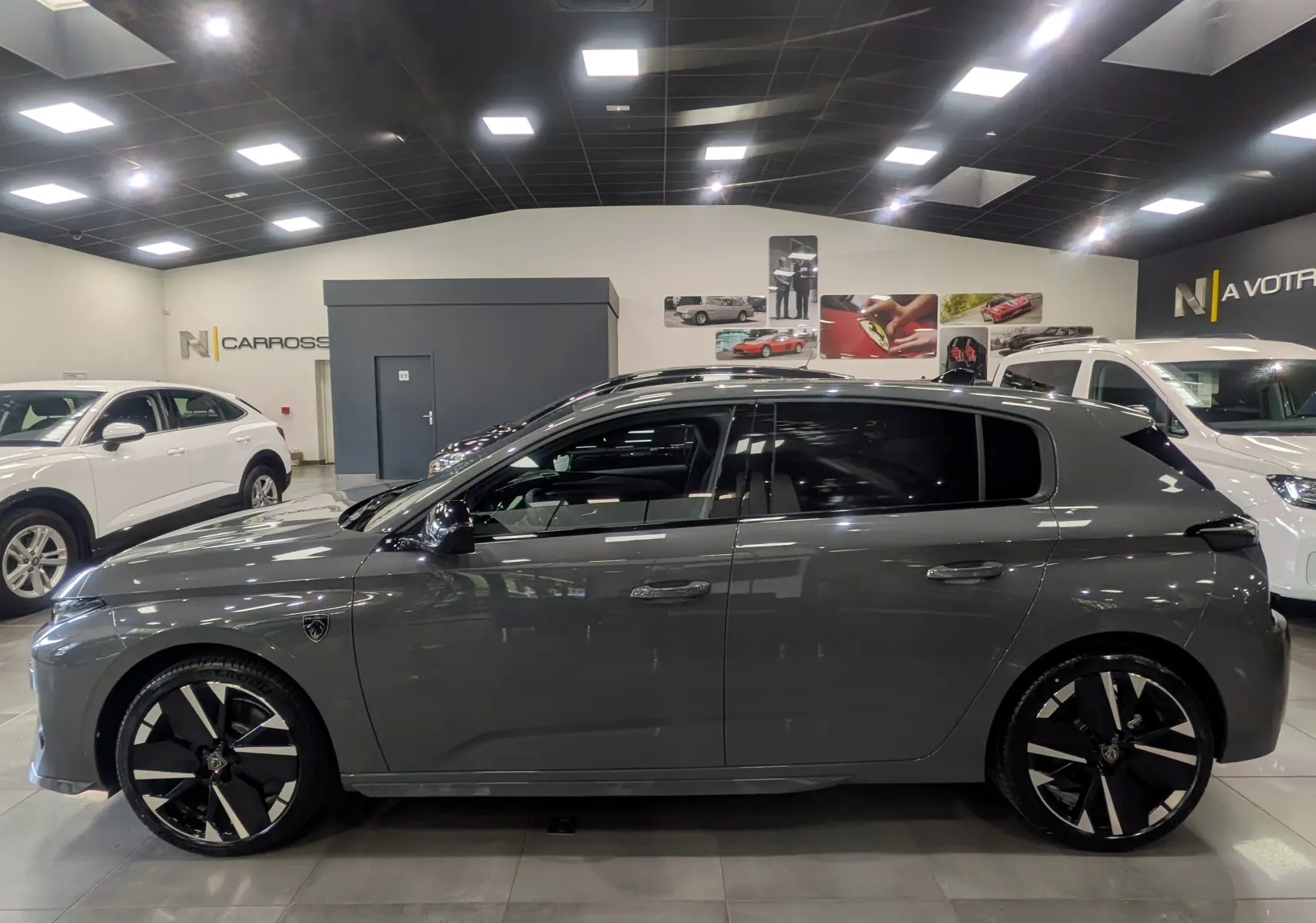 Peugeot 308 gris Sélénium vue de profil côté gauche, avec jantes noires et toit panoramique en intérieur showroom.