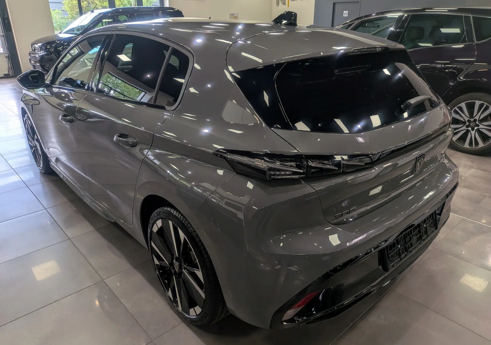 Vue 3/4 arrière droite d'une Peugeot 308 GT Exclusive gris Sélénium avec jantes bi-ton et vitres teintées en showroom.