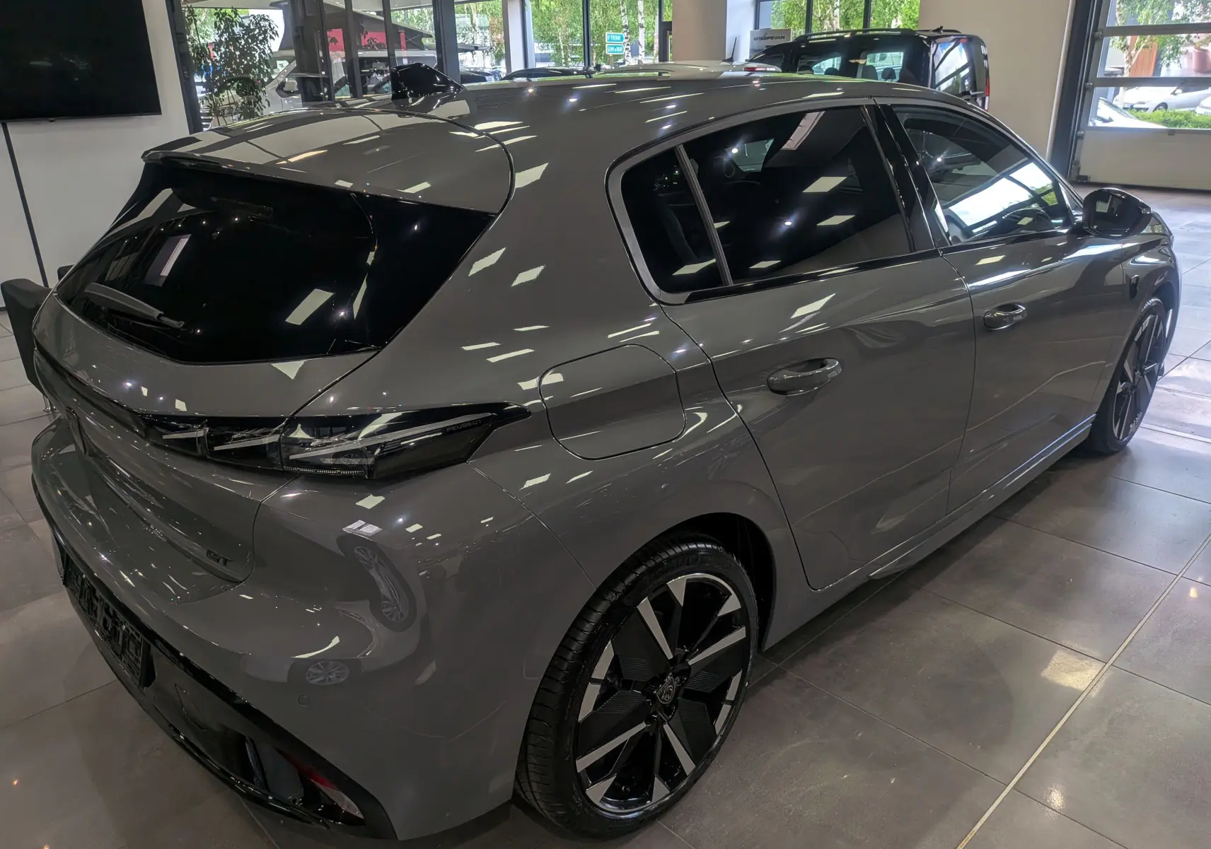 Vue 3/4 arrière droite d'une Peugeot 308 GT Exclusive gris Sélénium avec jantes noires bicolores et vitres teintées.