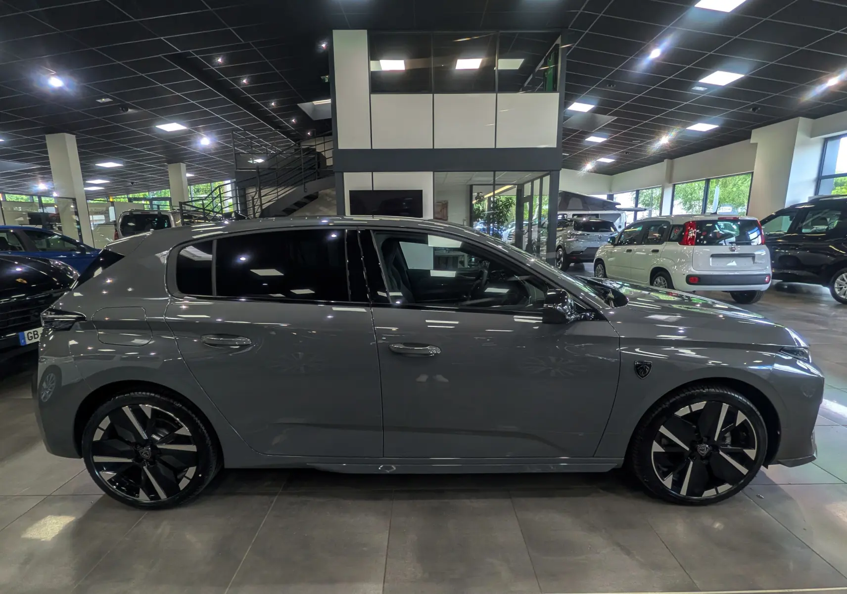 Vue de profil côté gauche d'une Peugeot 308 gris Sélénium avec jantes noires et toit noir dans un showroom.
