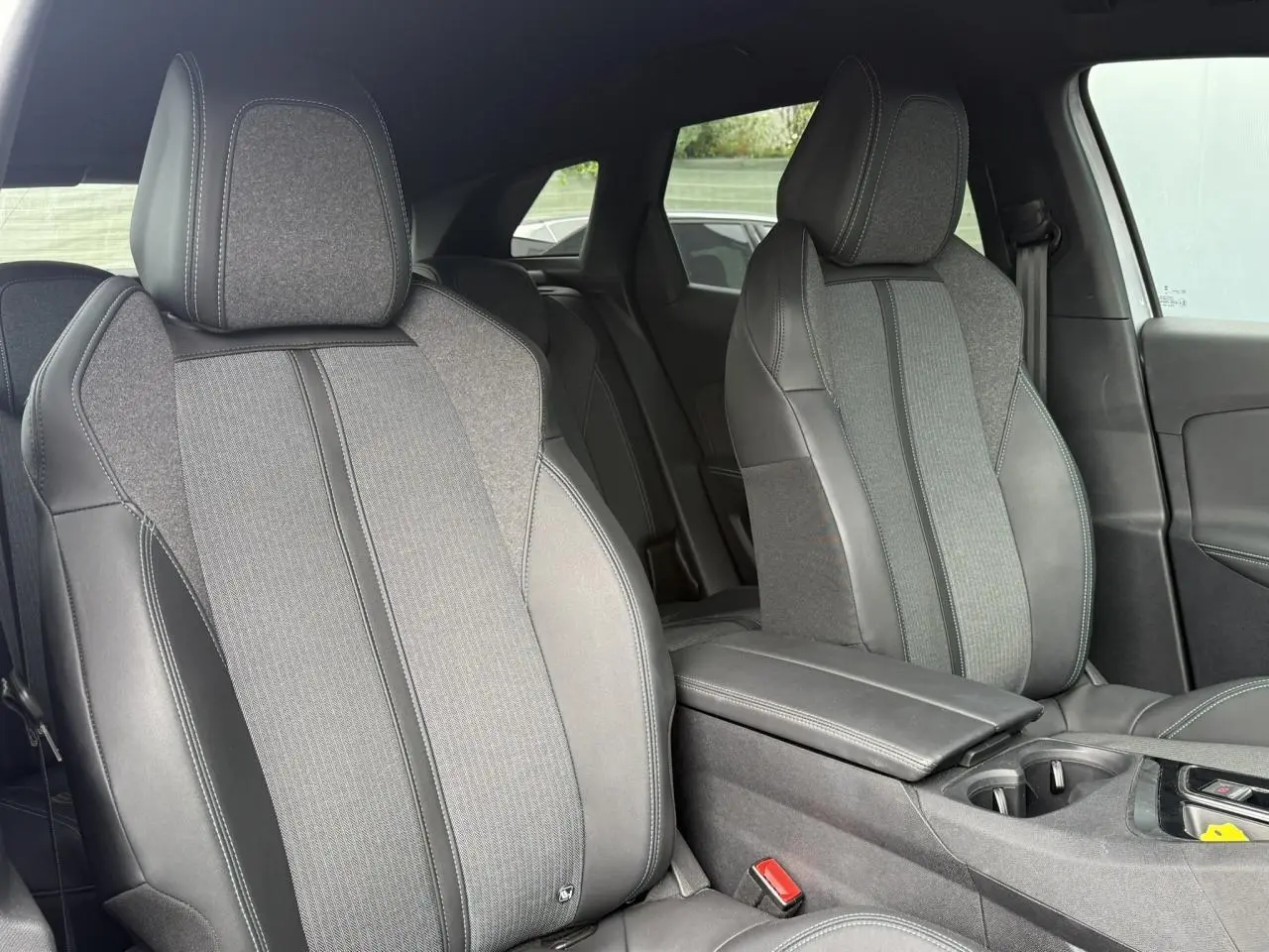 Vue intérieure rapprochée des sièges avant en tissu et cuir gris du Peugeot 3008 Plug-in Hybrid 2024 avec accoudoir central.