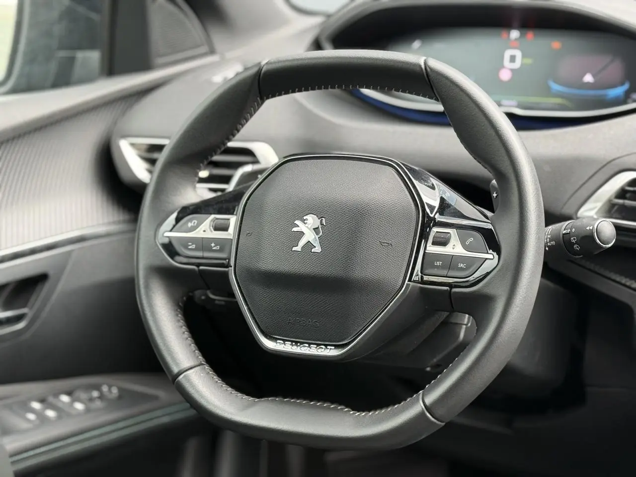 Volant compact cuir noir Mistral avec logo Peugeot au centre, tableau de bord et commandes intégrées visibles en arrière-plan.