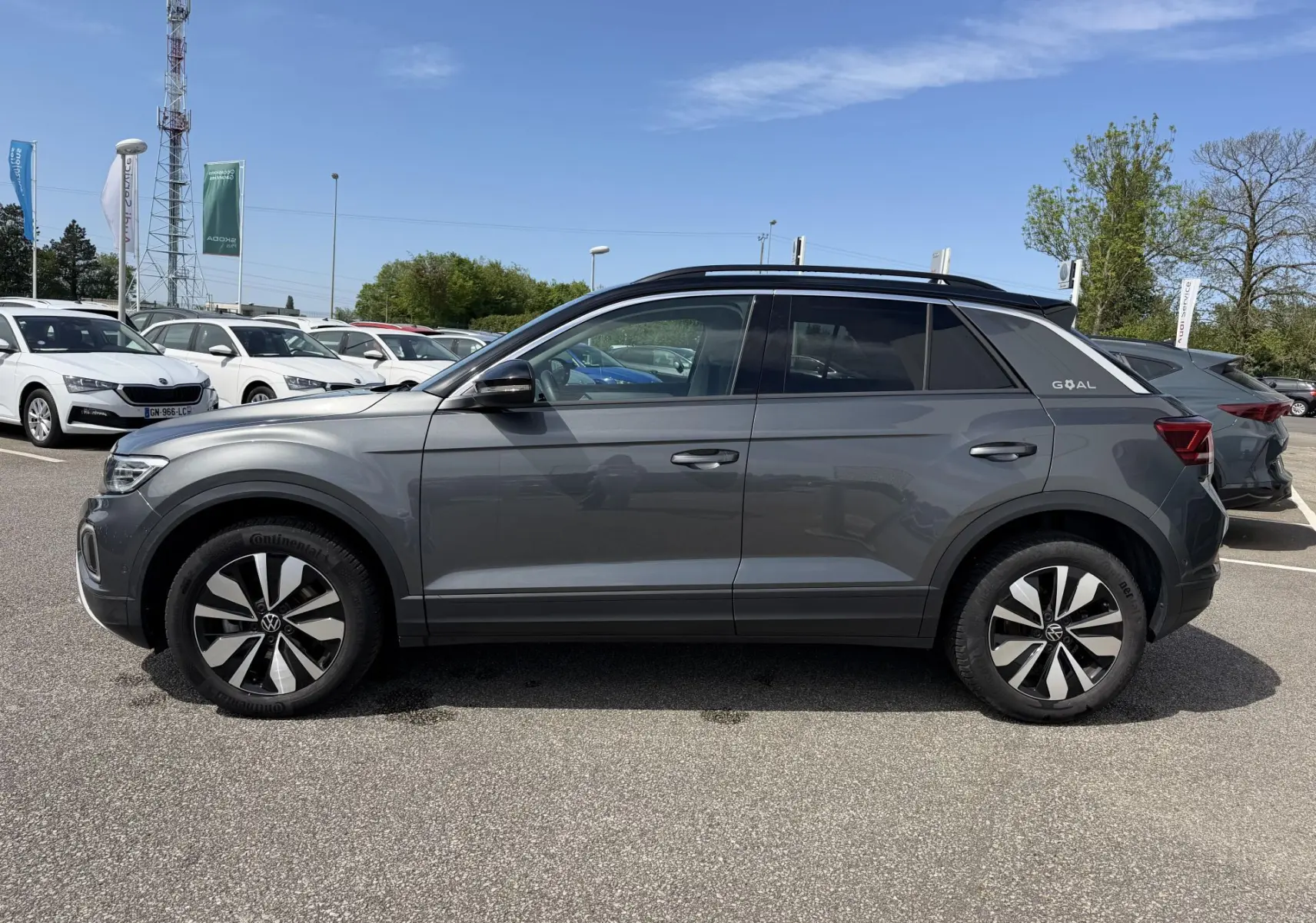 Profil droit d'un Volkswagen T-Roc gris 2025 avec barres de toit noires et jantes distinctives en alliage.