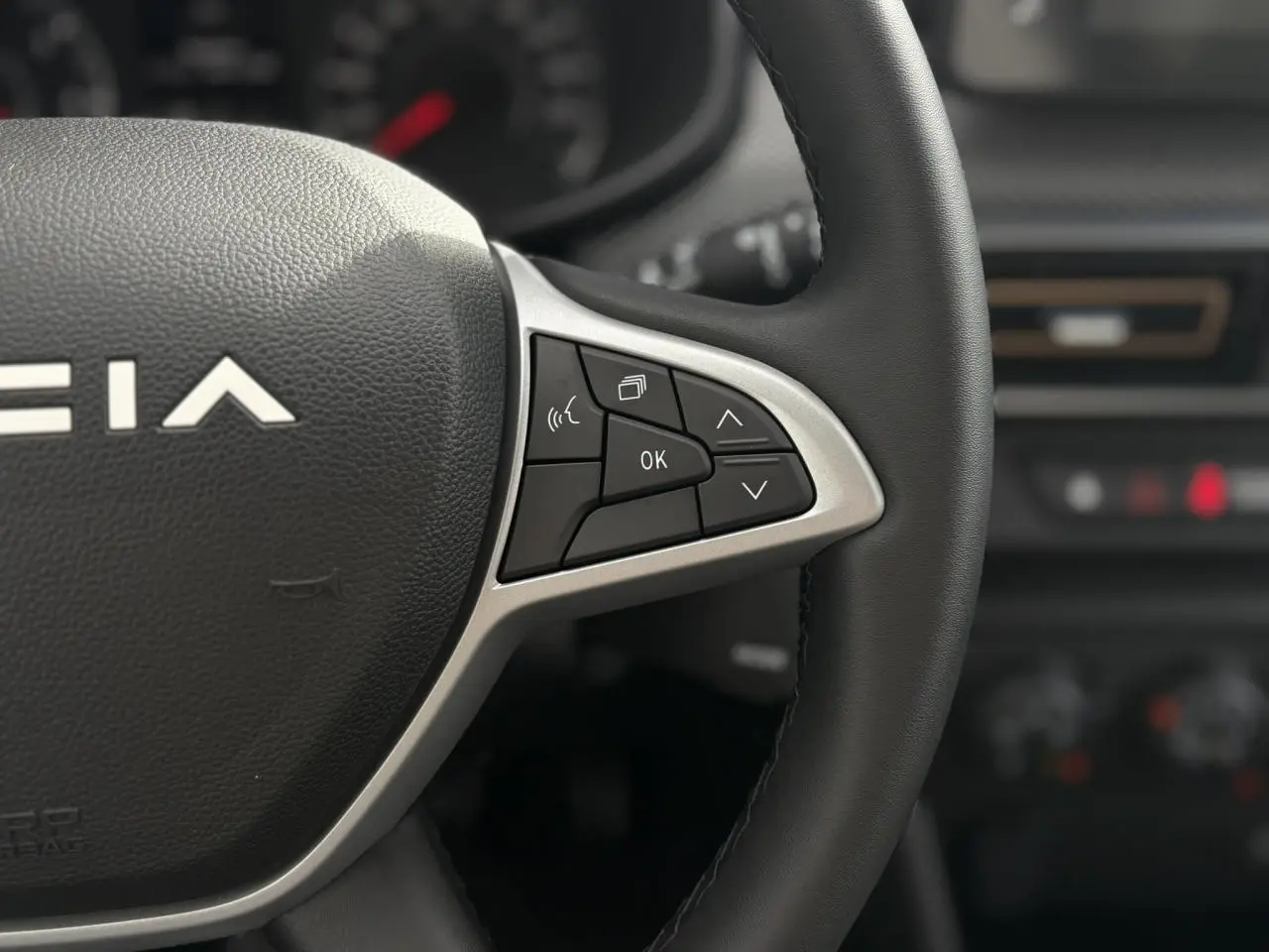 Gros plan sur les commandes du volant Soft Feel noir de la Dacia Sandero Stepway 2025, intérieur sombre flou en arrière-plan