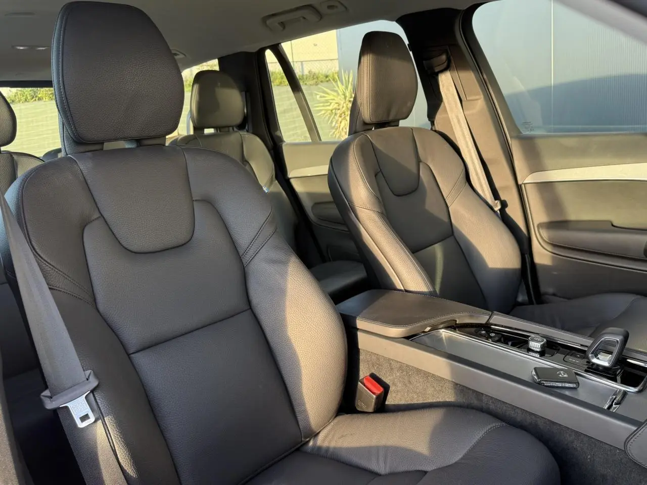 Vue intérieure sur les sièges avant en cuir noir du Volvo XC90 2024, avec accoudoir central et console moderne.
