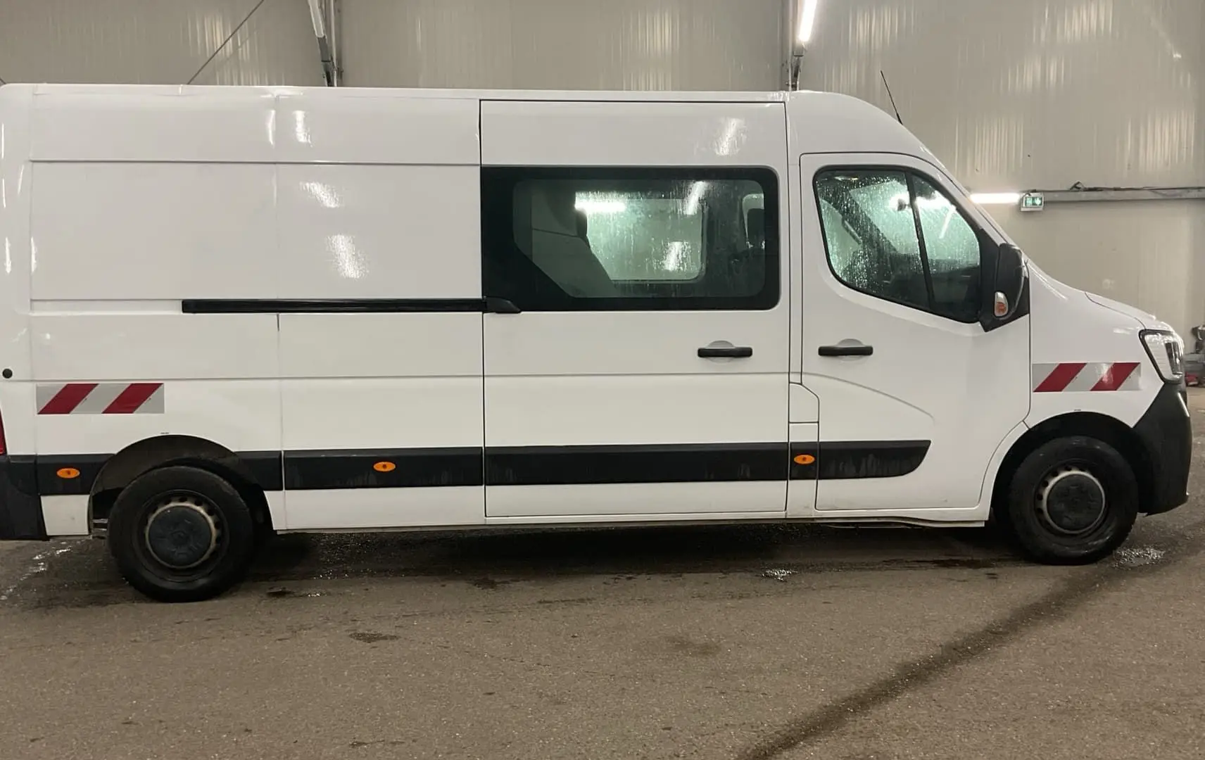 Vue latérale droite d’un Renault Master cabine approfondie blanc avec marquages rouges réfléchissants et vitres teintées.