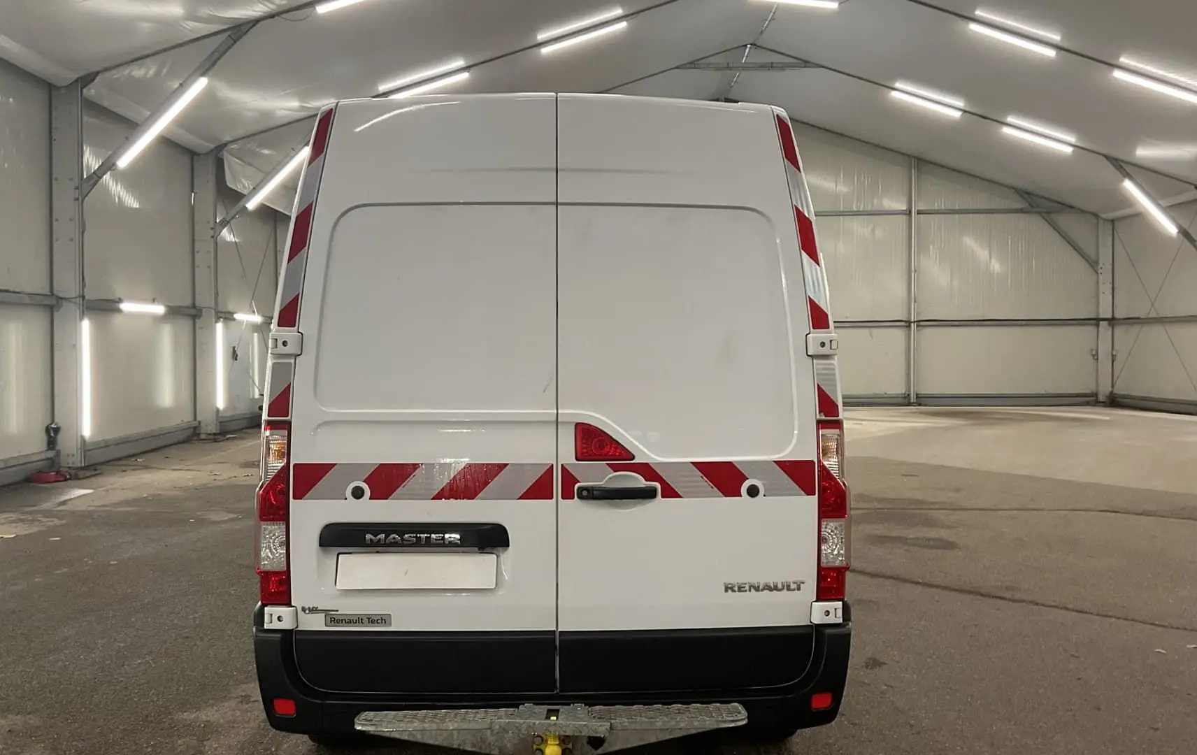Vue arrière d’un Renault Master blanc avec bandes réfléchissantes rouges et blanches dans un grand hangar.