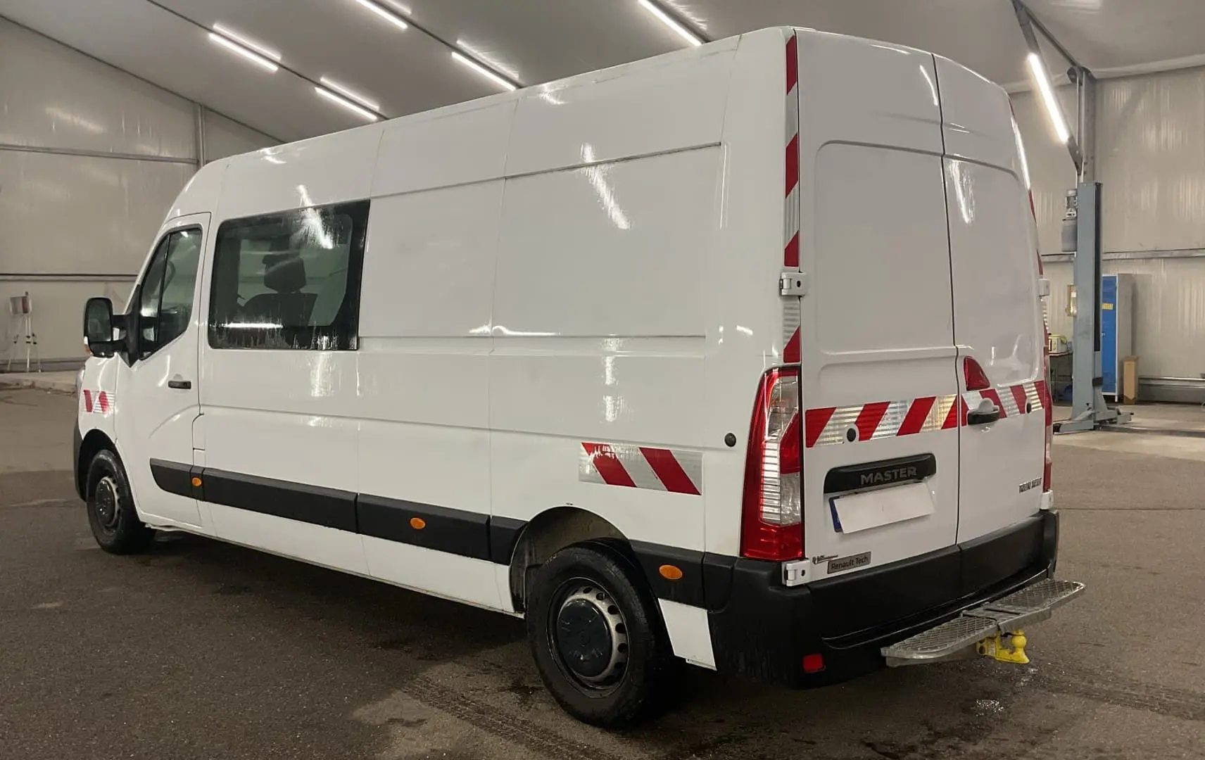 Vue 3/4 arrière droite d’un Renault Master blanc avec marquages réfléchissants rouges et blancs en intérieur d’atelier.