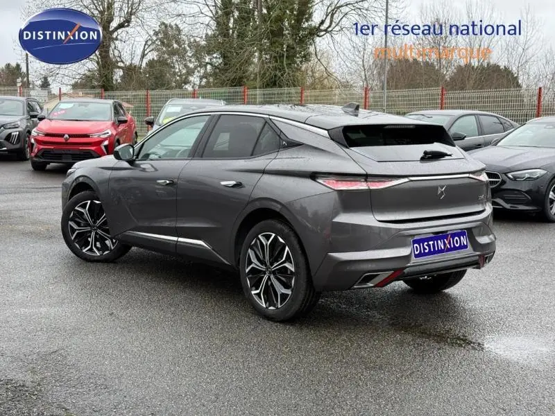 Vue 3/4 arrière droite d'une DS4 2023 Gris Platinium avec jantes noires et design dynamique, stationnée sur un parking humide.