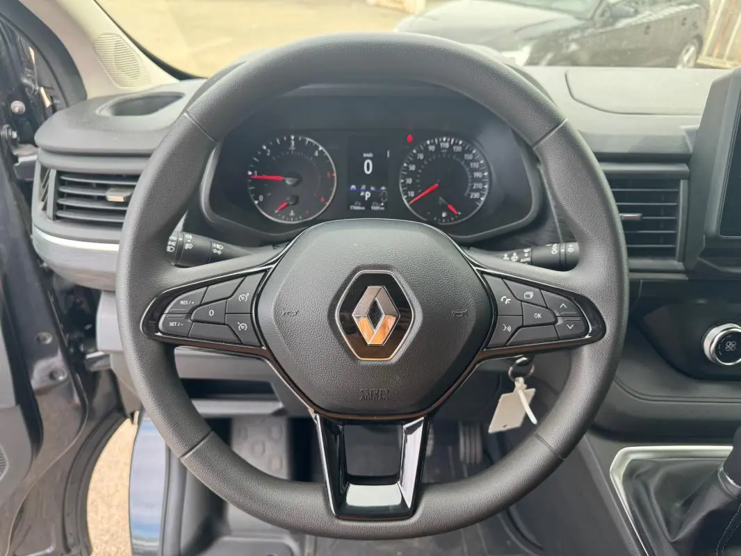 Vue rapprochée du volant noir avec logo Renault du Trafic Fourgon gris foncé, tableau de bord et commandes visibles.