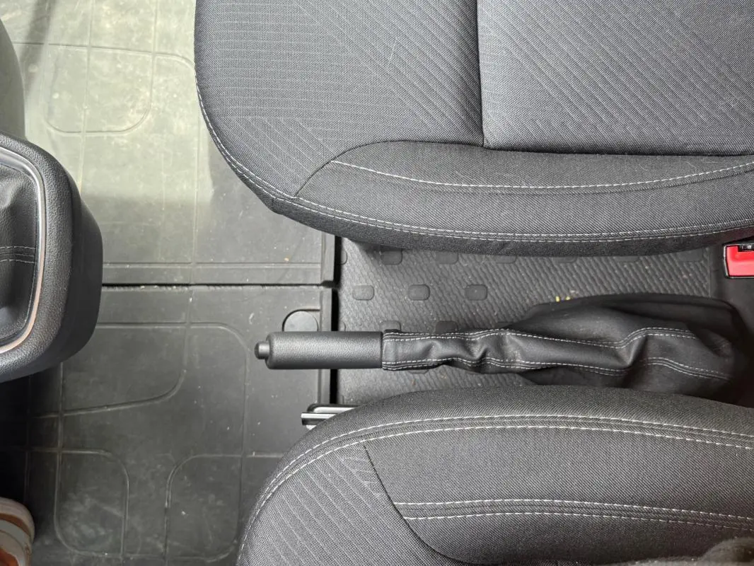Vue rapprochée de la poignée de frein à main entre les sièges avant gris foncé du Renault Trafic Fourgon 2024.