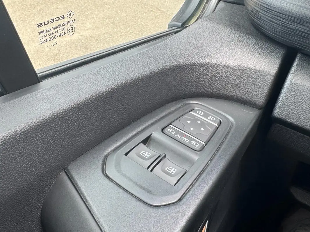 Gros plan sur les commandes électriques des vitres et rétroviseurs côté conducteur du Renault Trafic Fourgon gris foncé.
