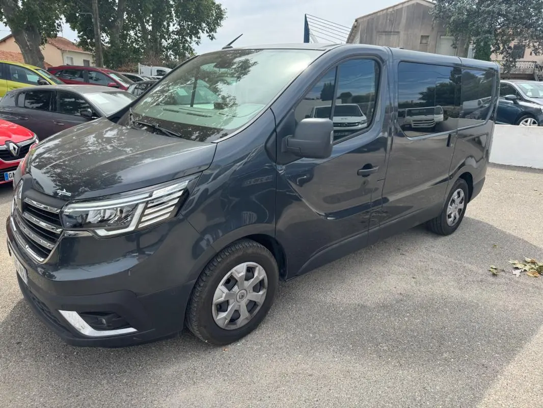 Renault Trafic Fourgon gris foncé en 3/4 avant droit, avec vitres surteintées et porte latérale visible.