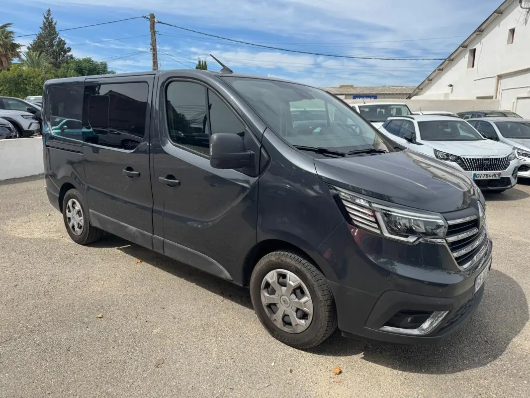 Renault Trafic Fourgon gris foncé en 3/4 avant droit, avec vitres surteintées et porte latérale visible.