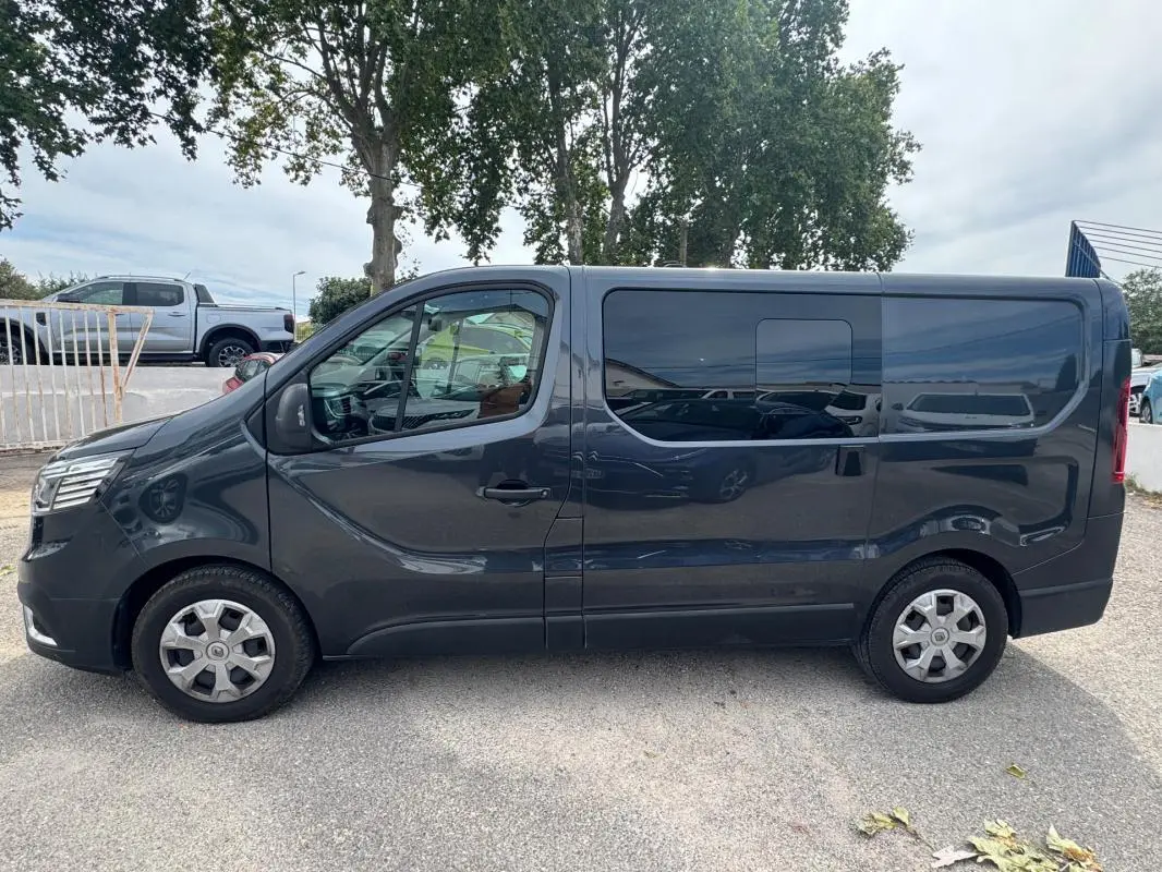 Profil côté gauche d'un Renault Trafic Fourgon gris foncé avec porte latérale et vitres surteintées.