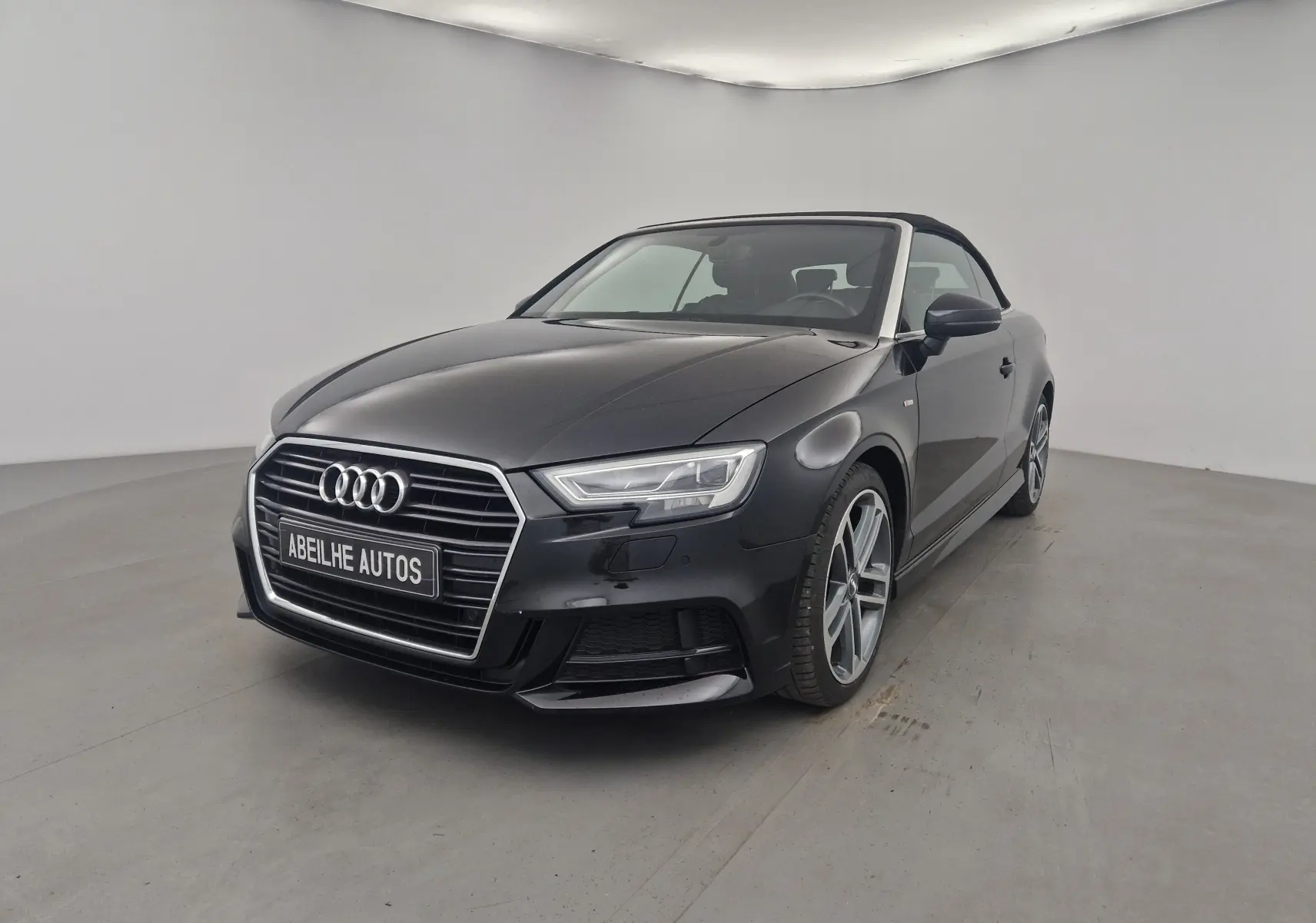 Audi A3 Cabriolet noir vue 3/4 avant droit avec capote en toile fermée dans un studio lumineux.
