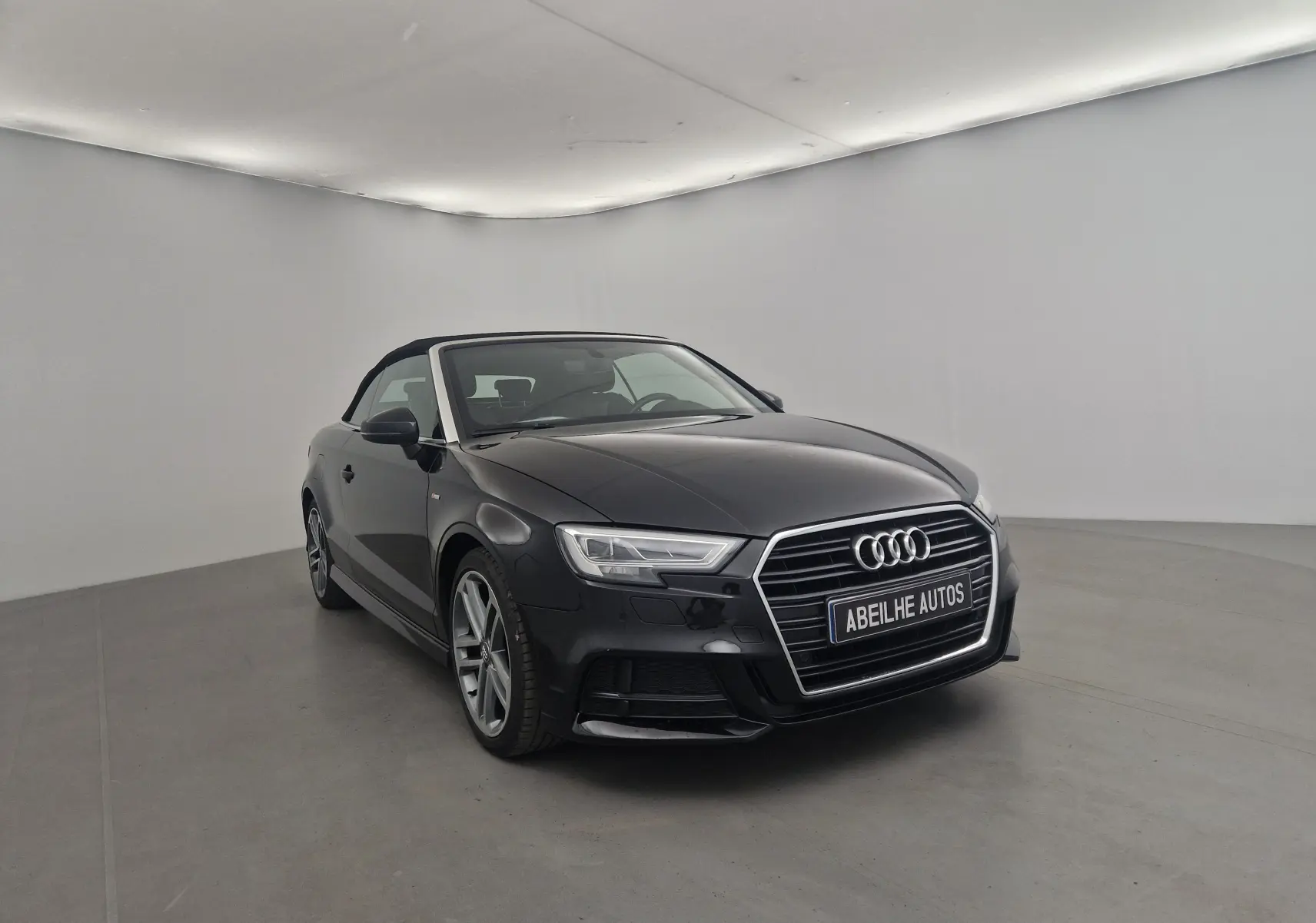 Audi A3 Cabriolet noir vue 3/4 avant avec capote en toile fermée dans un studio lumineux.