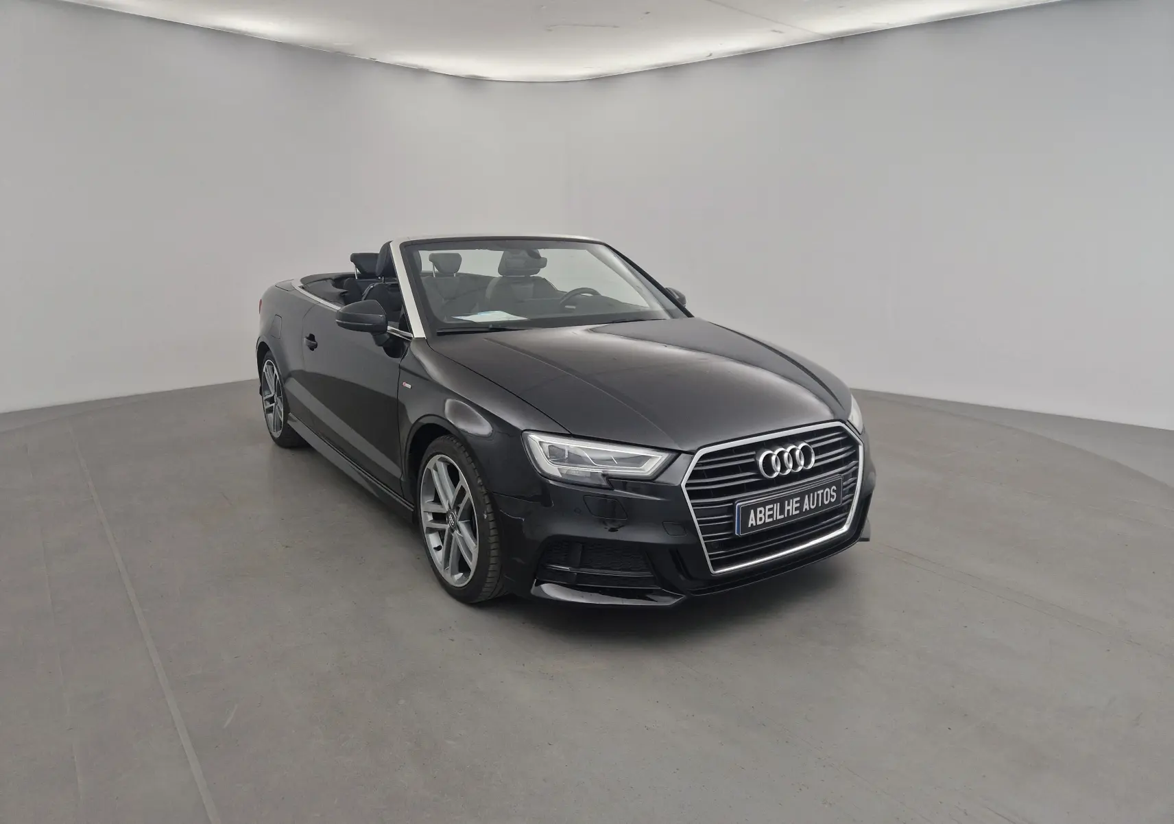 Audi A3 Cabriolet noir vue 3/4 avant droit, capote ouverte, intérieur cuir noir et jantes alliage 18 pouces.