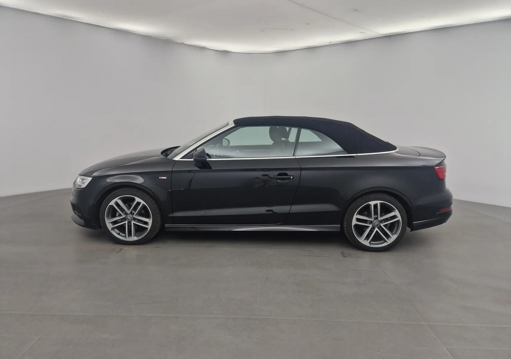 Profil côté gauche d'une Audi A3 Cabriolet noire avec capote en toile fermée et jantes alliage 18 pouces S-Line.