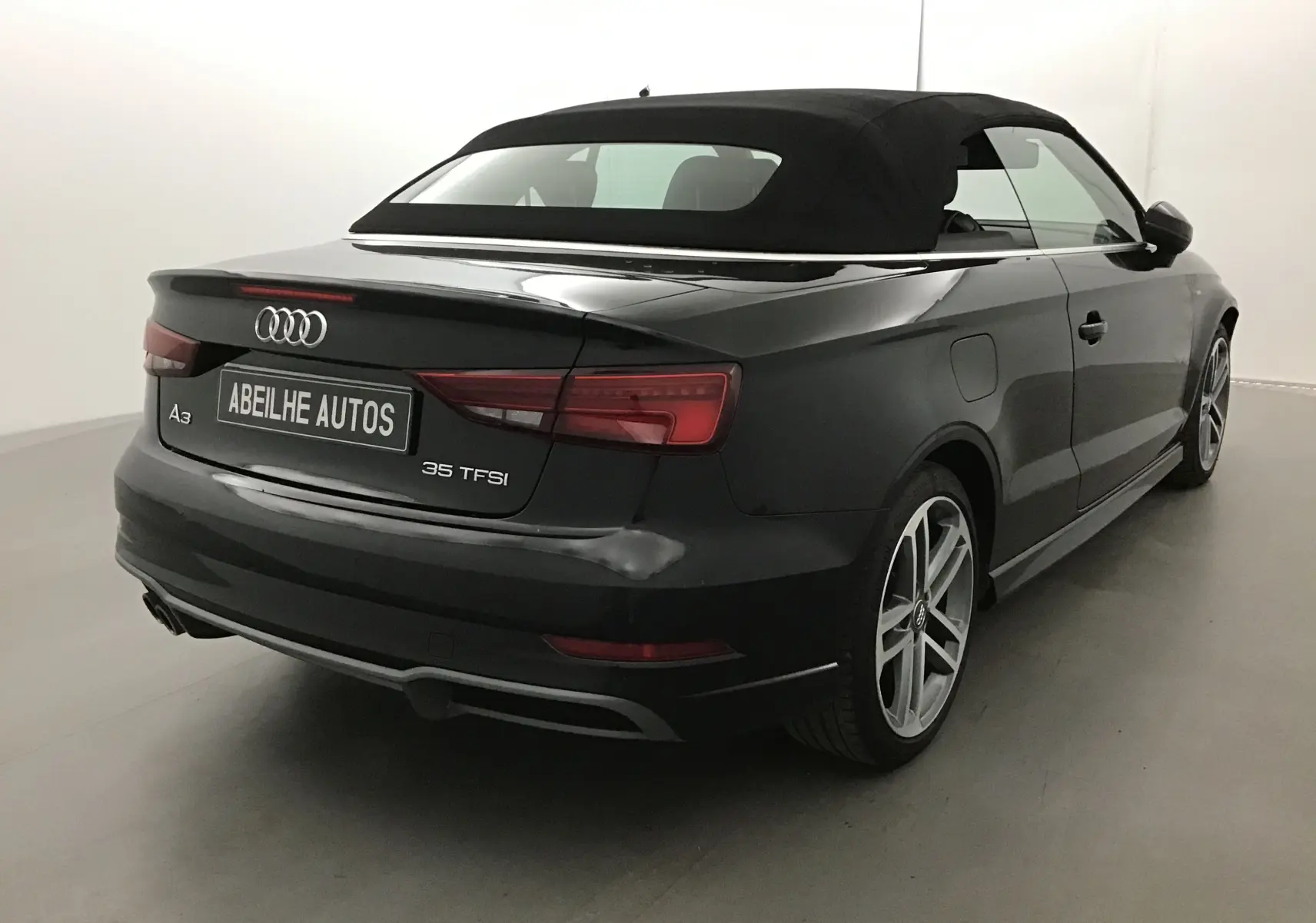 Vue 3/4 arrière droite d'une Audi A3 Cabriolet noire avec capote en toile fermée dans un studio lumineux.