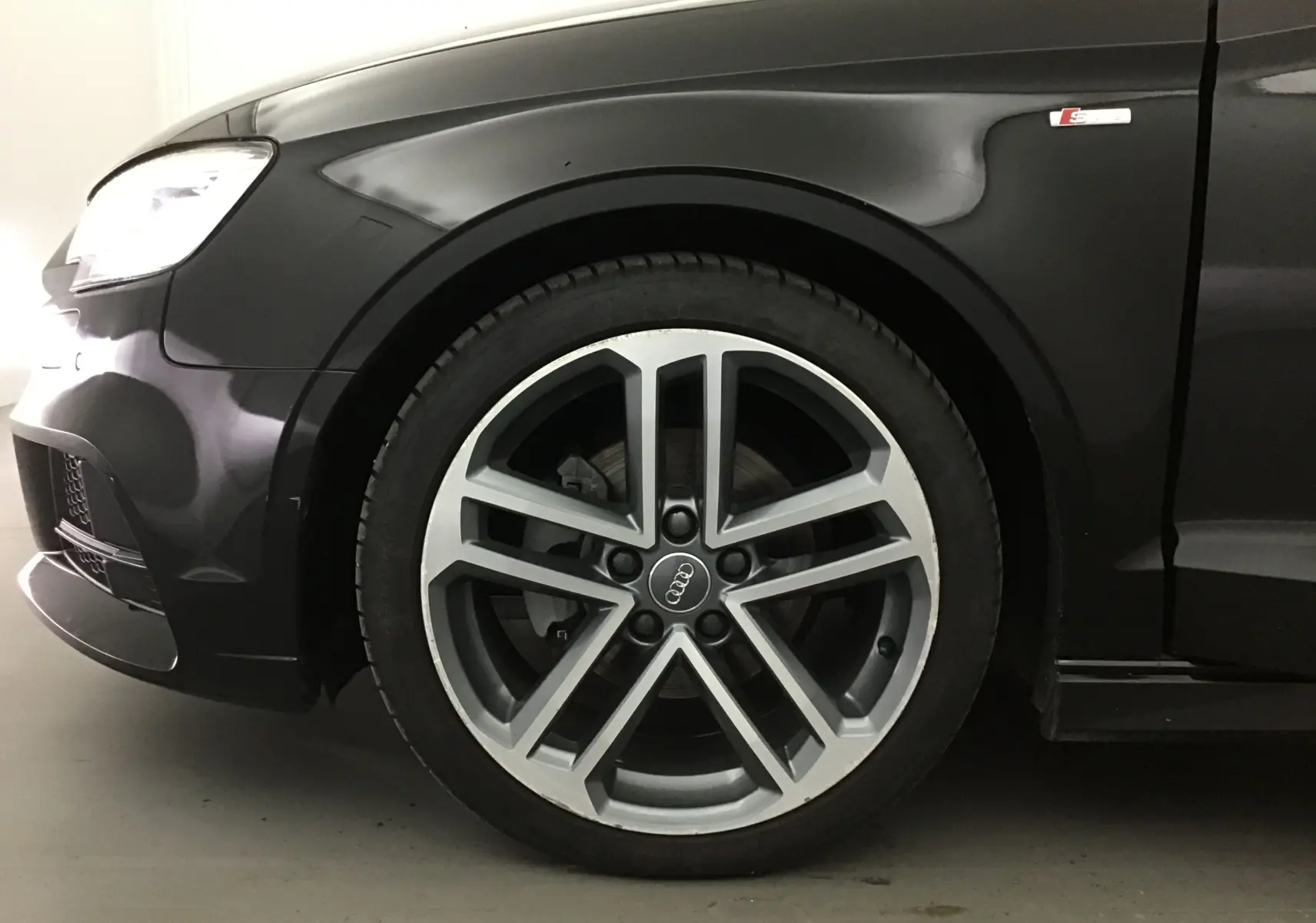 Gros plan sur la roue avant gauche et l'aile noire d'une Audi A3 Cabriolet 1.5 TFSI S-Line avec logo S visible.