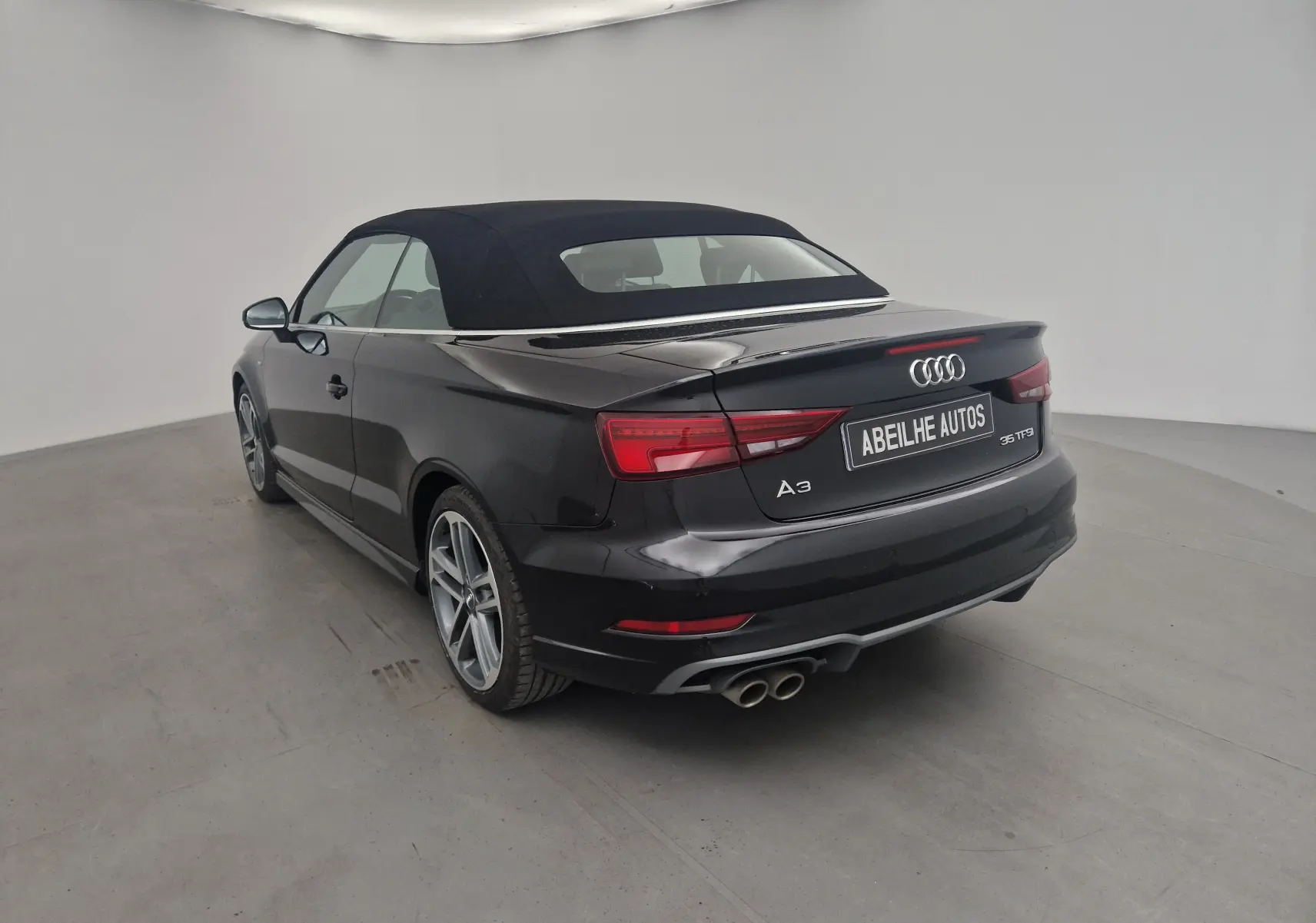 Audi A3 Cabriolet noir vue 3/4 arrière droit avec capote en toile fermée et double sortie d'échappement chrome.