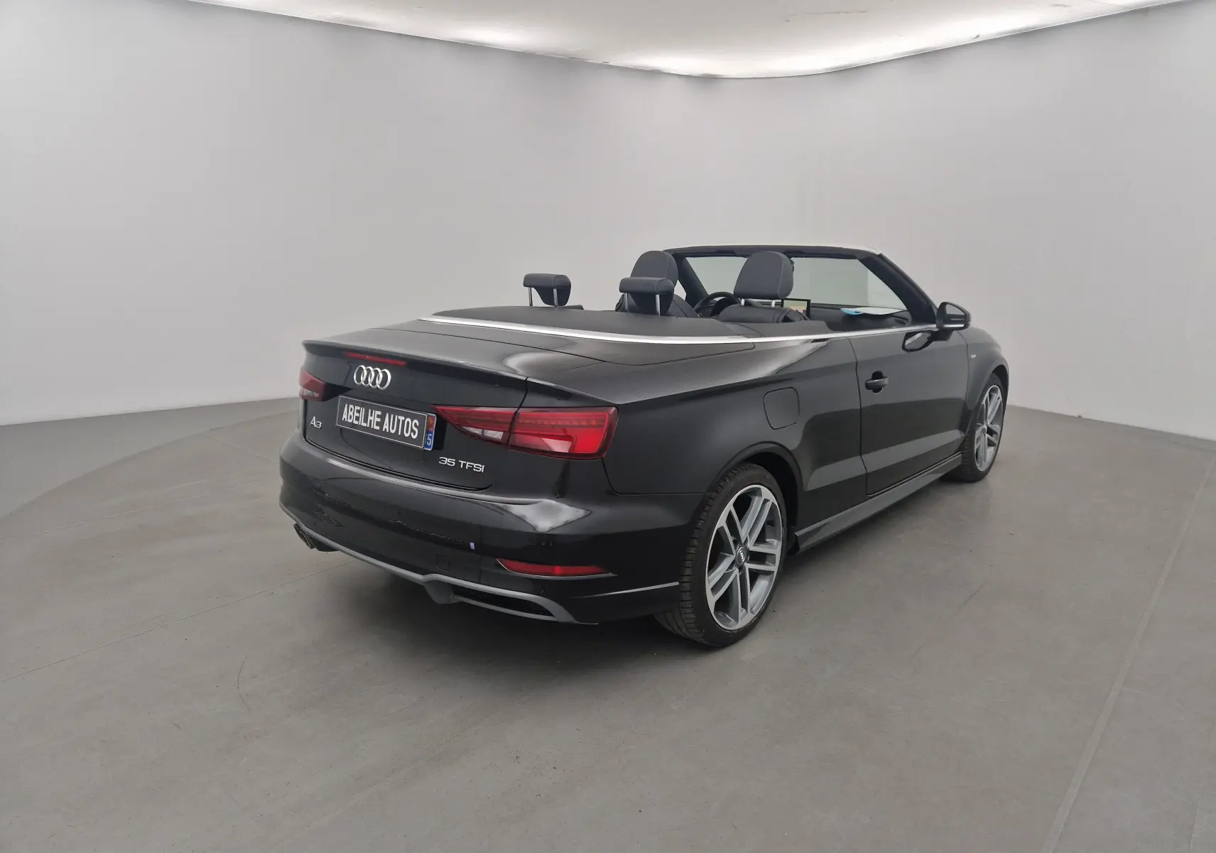 Audi A3 Cabriolet noir vue 3/4 arrière droit, capote électrique repliée et jantes alliage 18 pouces visibles.
