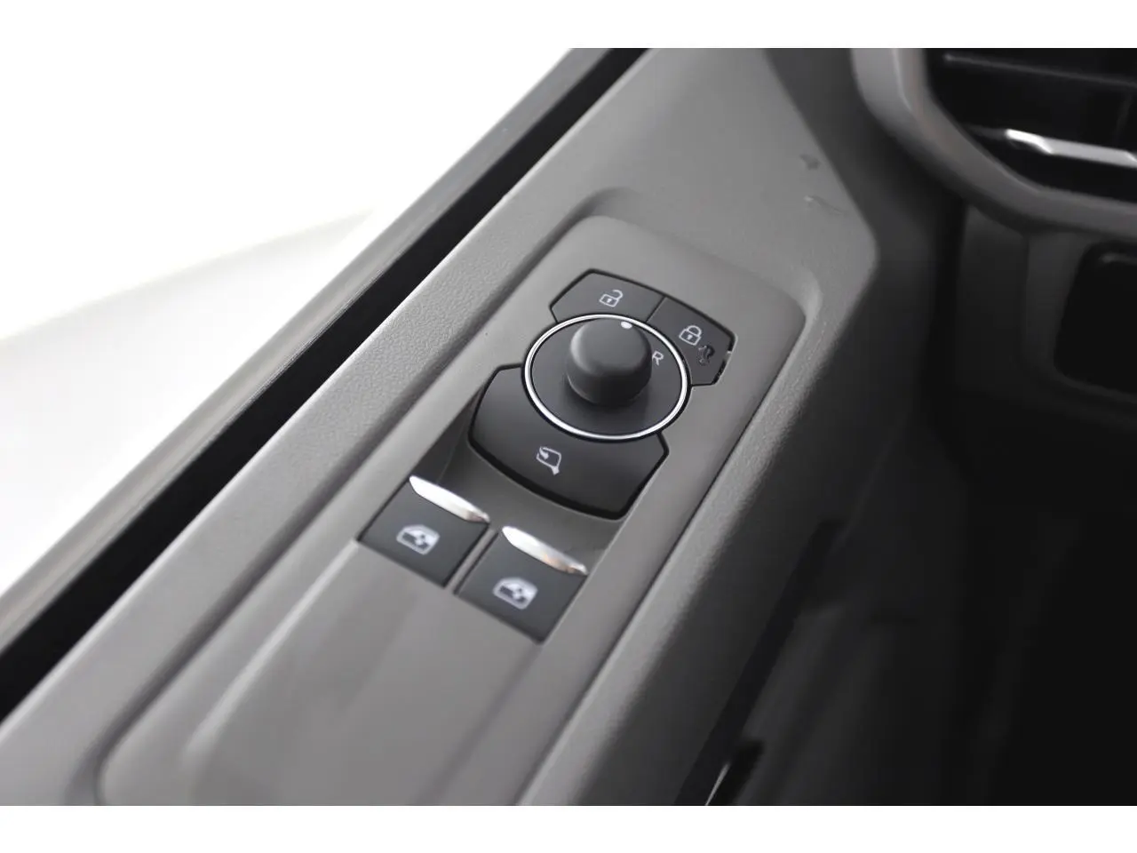 Gros plan sur les commandes de réglage des rétroviseurs et vitres côté conducteur du Volkswagen Transporter gris Stone 2025.